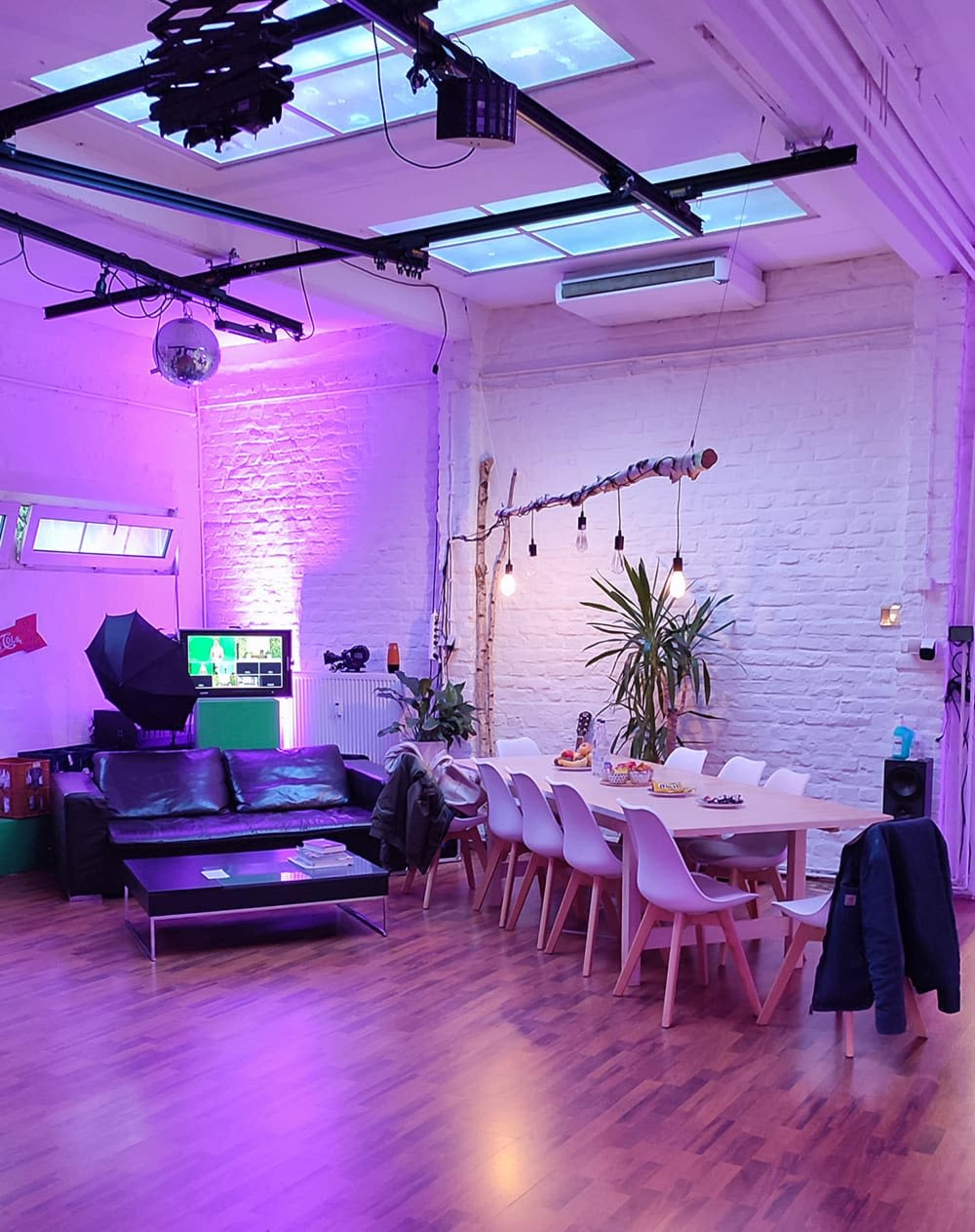 The image shows an interior space with a modern seating area featuring a black sofa, a dining table surrounded by white chairs, and colorful lighting accents on the walls and ceiling.