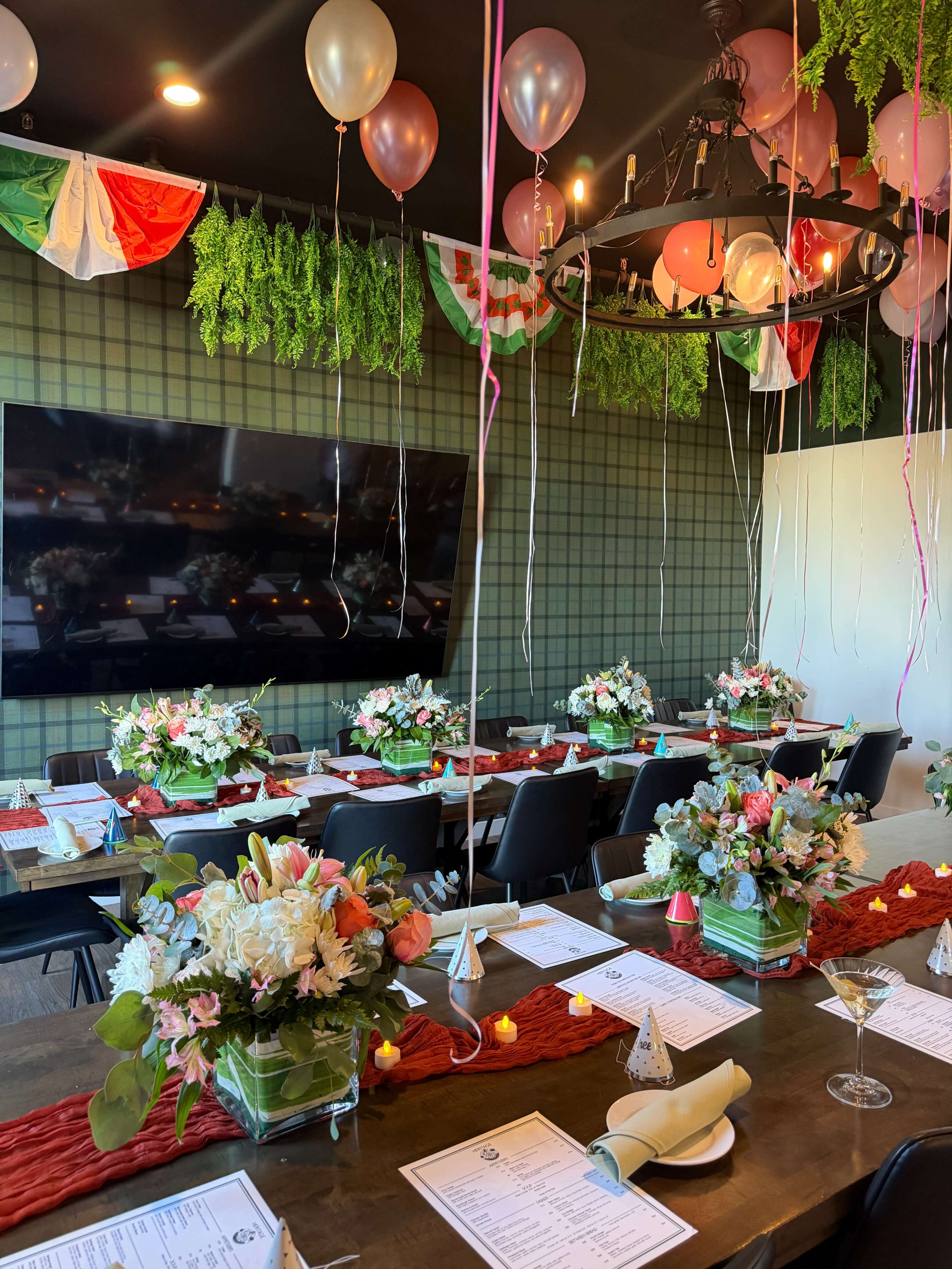 A dining area is elegantly decorated with flower arrangements, balloons, and festive banners, set for a special event.