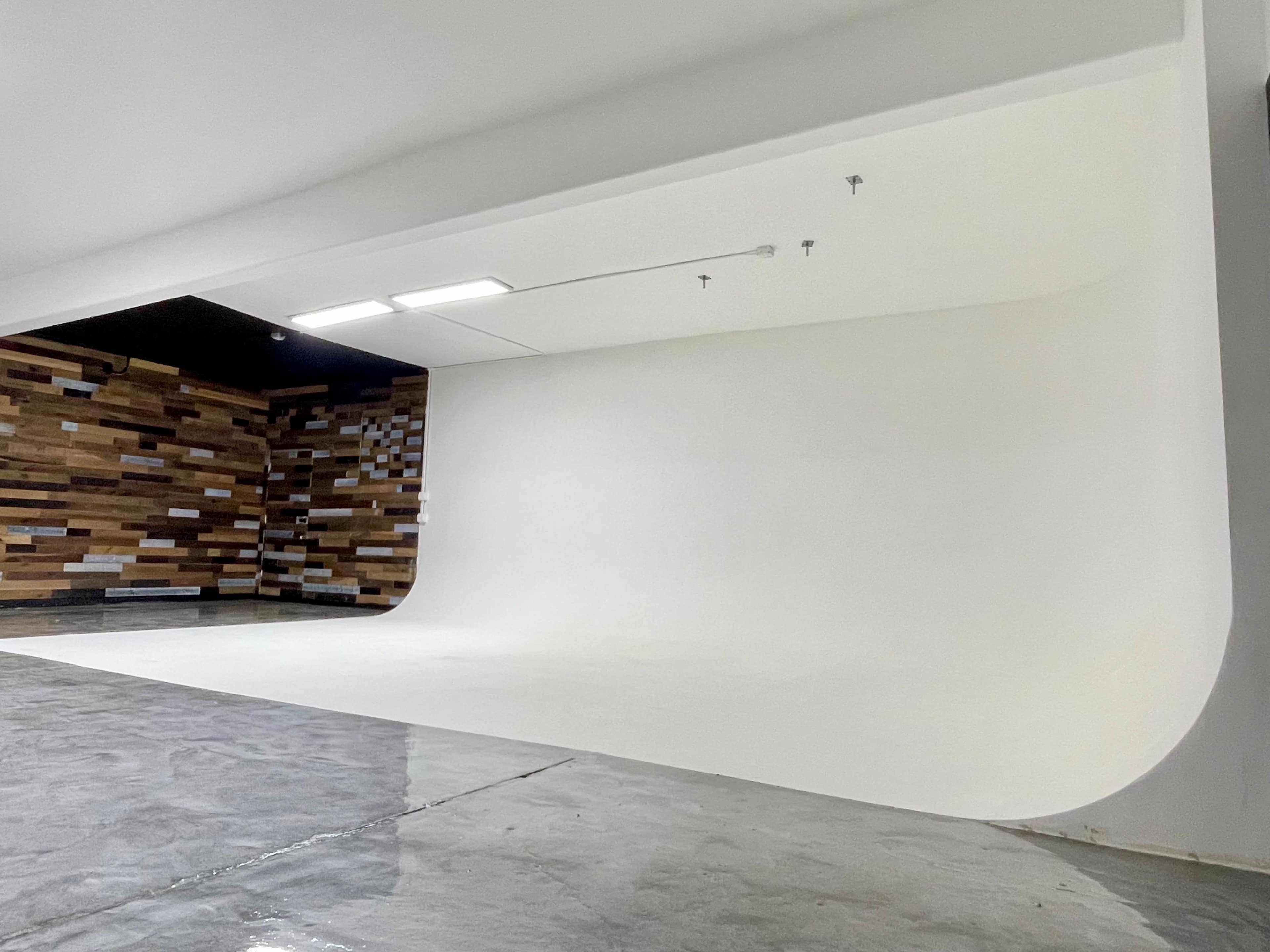 The image shows a spacious photography studio featuring a seamless white backdrop and a wooden accent wall.