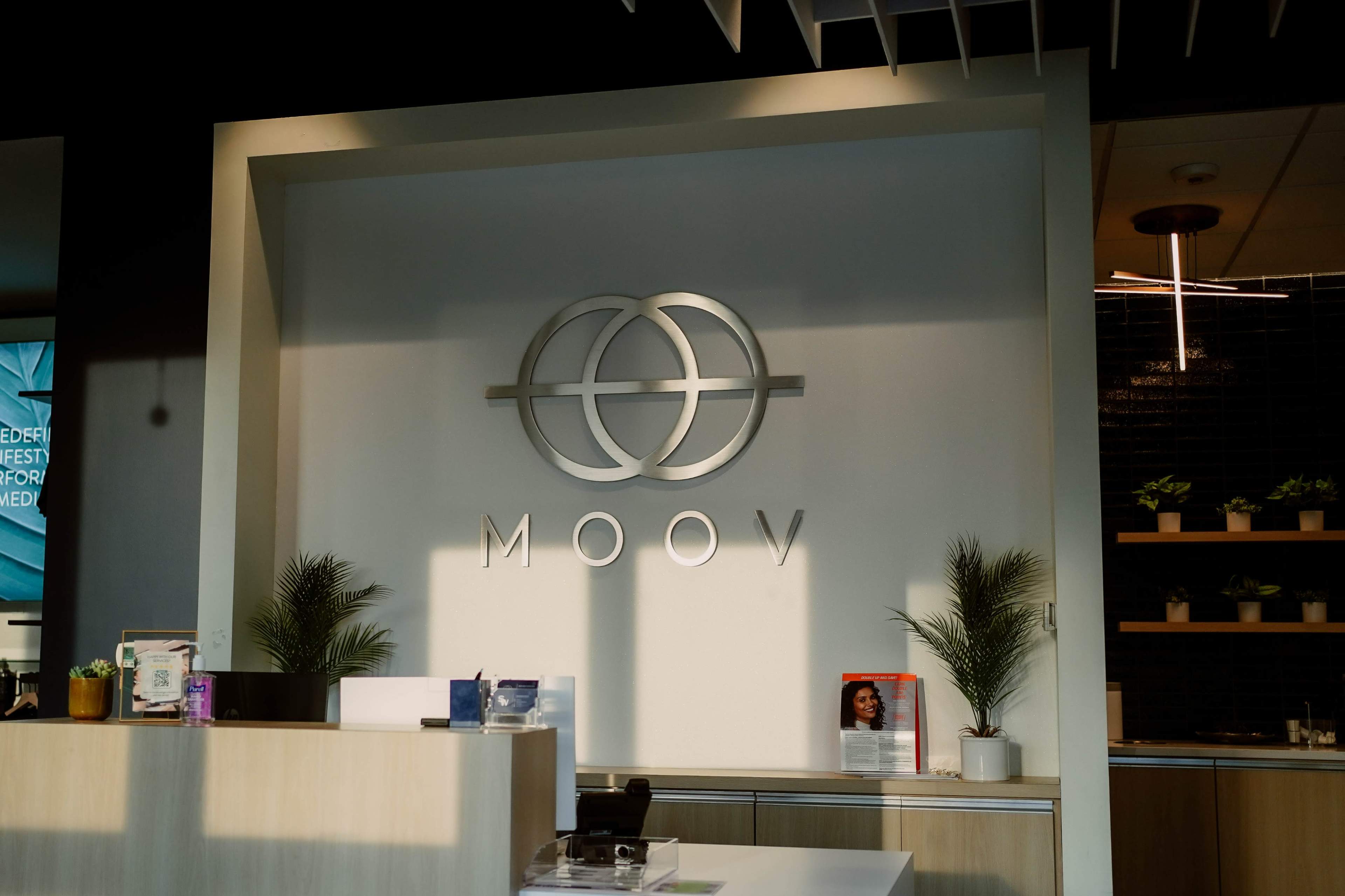 The image shows a modern reception area with a logo featuring overlapping circles and the word "MOOV" prominently displayed on the wall.