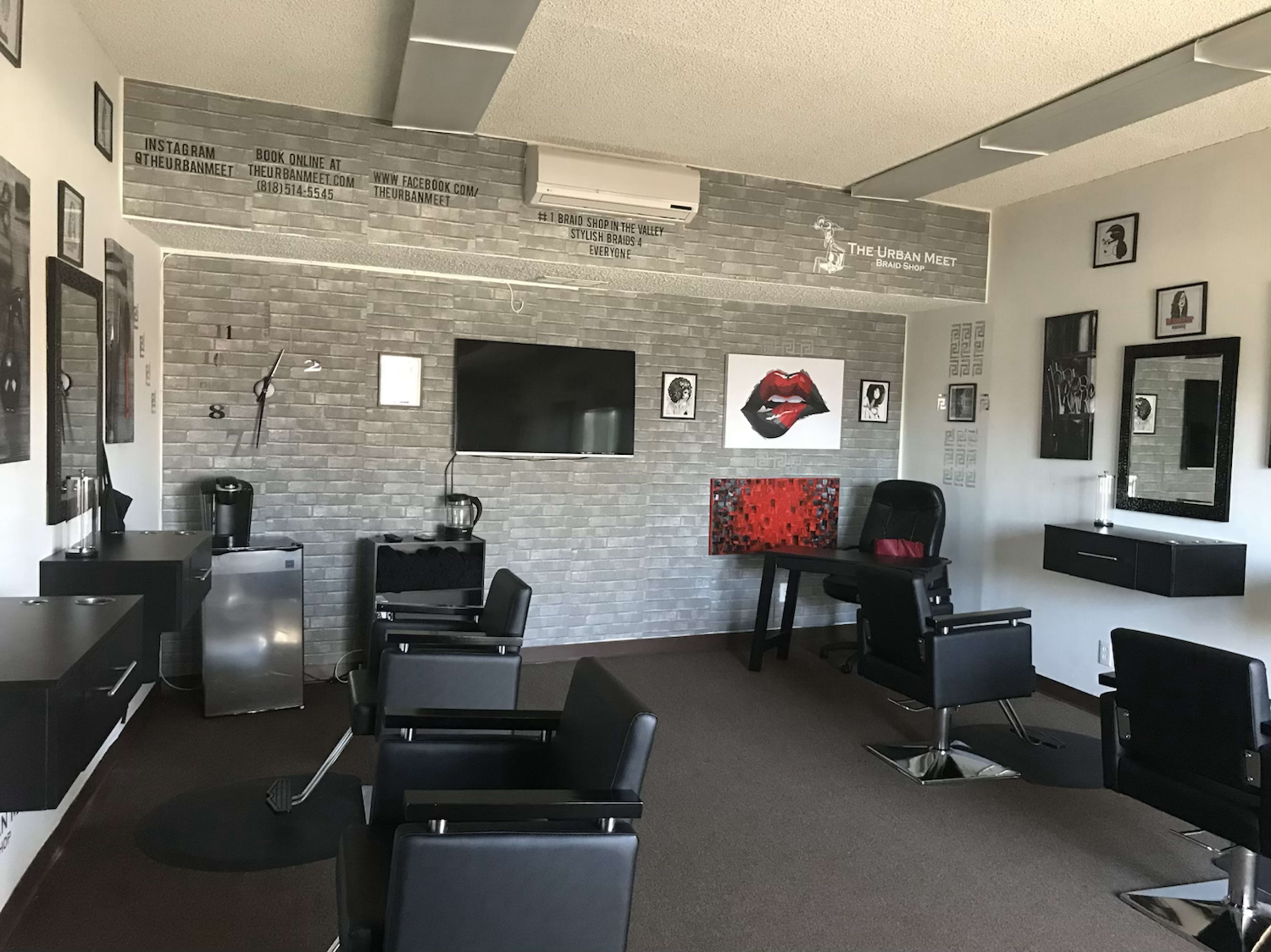 The interior of a modern hair salon featuring black chairs, a flat-screen television on the wall, and various artistic decorations.