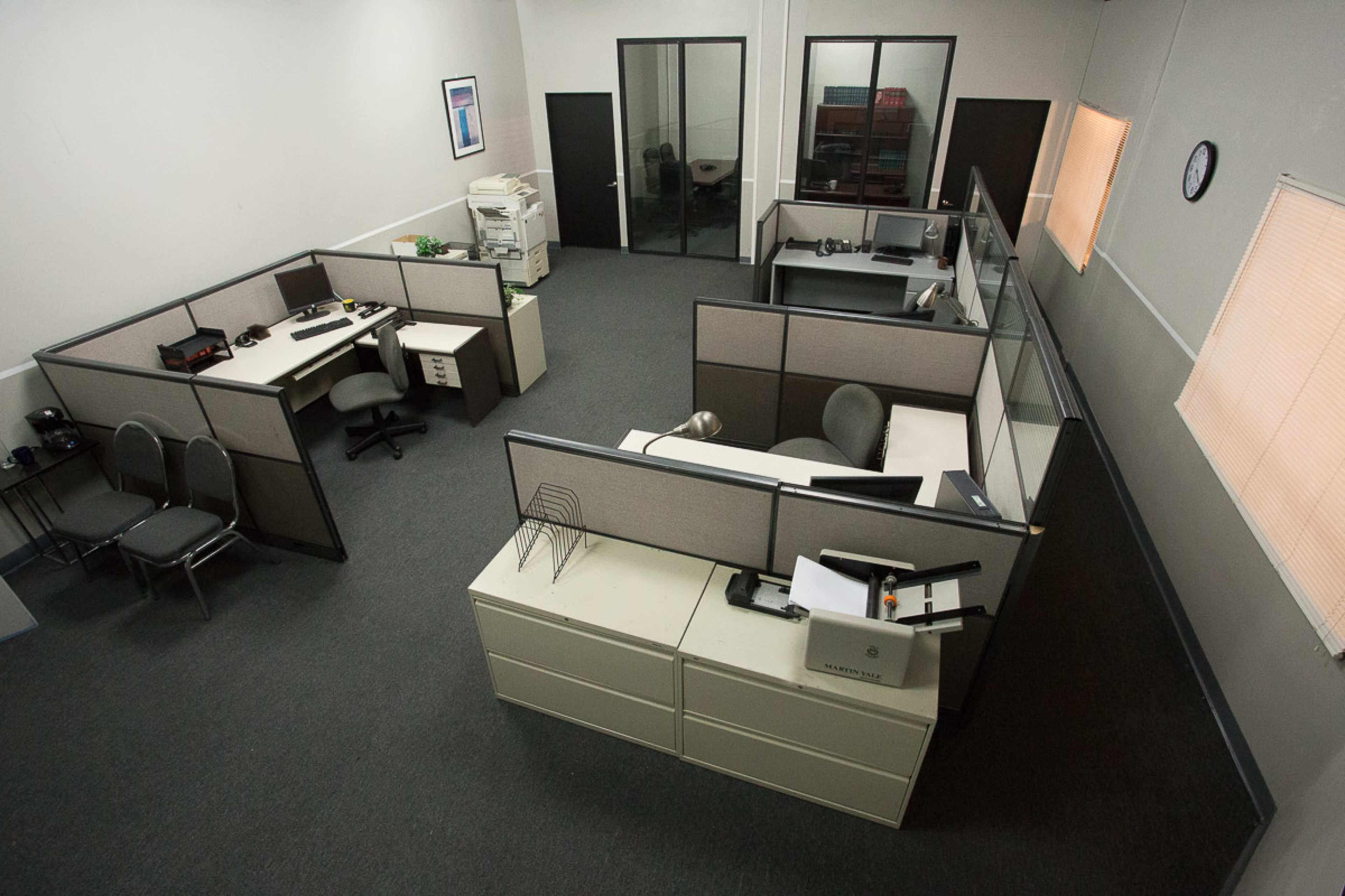 An office space with several cubicles, desks, and office equipment, arranged in a rectangular layout.