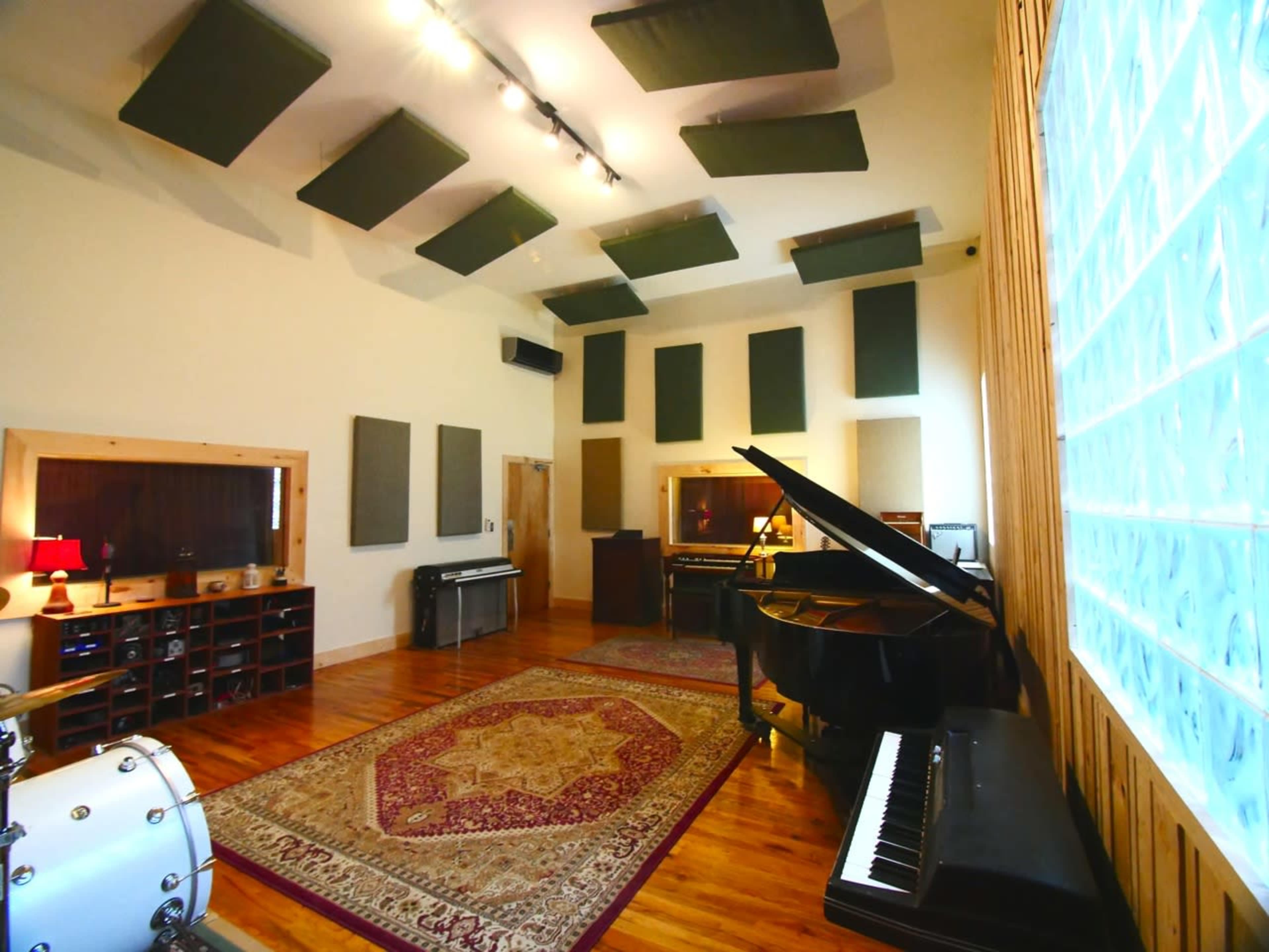 A spacious music studio equipped with a grand piano, a drum set, and various soundproofing panels on the walls.