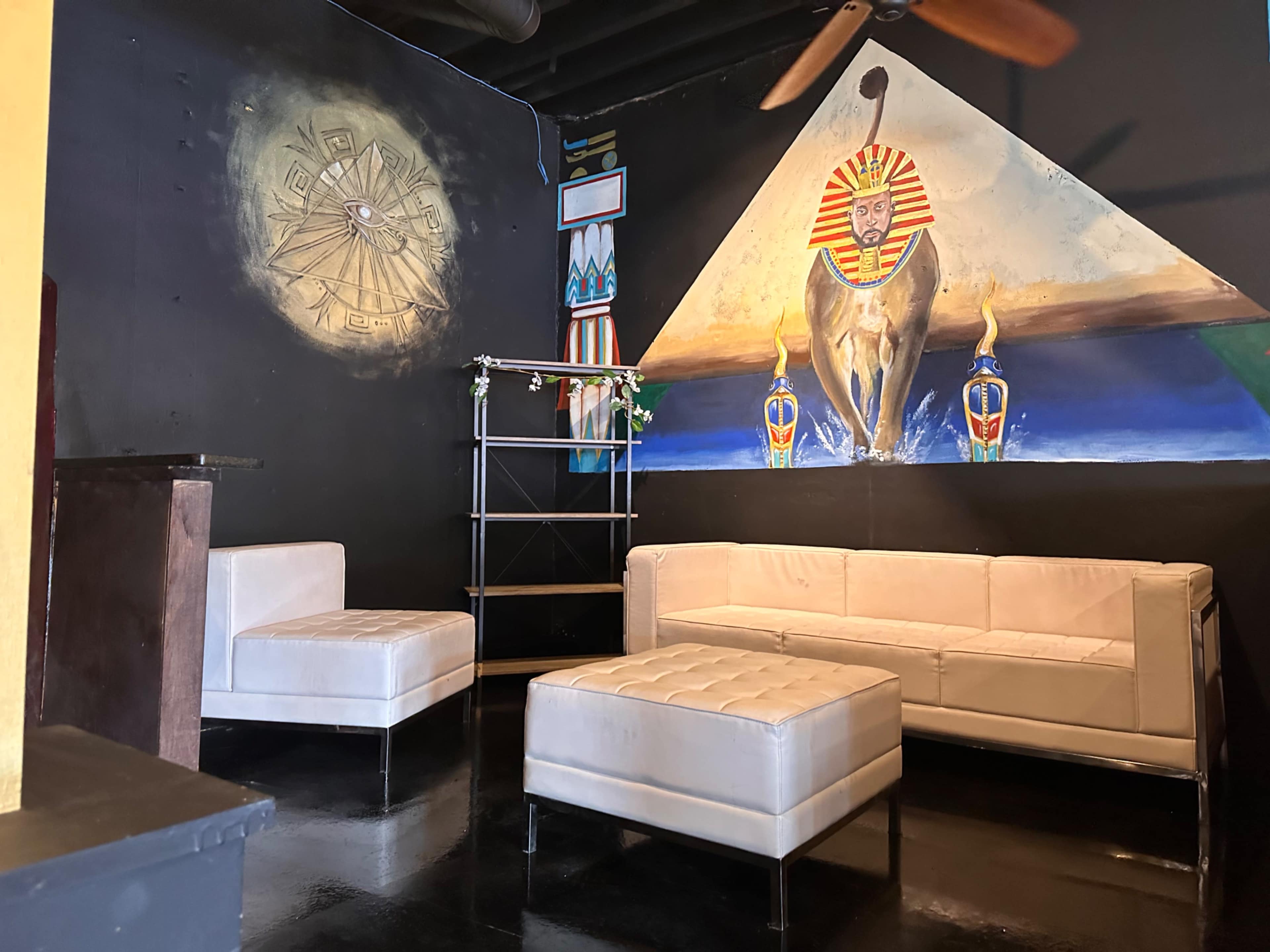A lounge area with white furniture, featuring an artistic mural of a lion and Egyptian motifs on the wall.