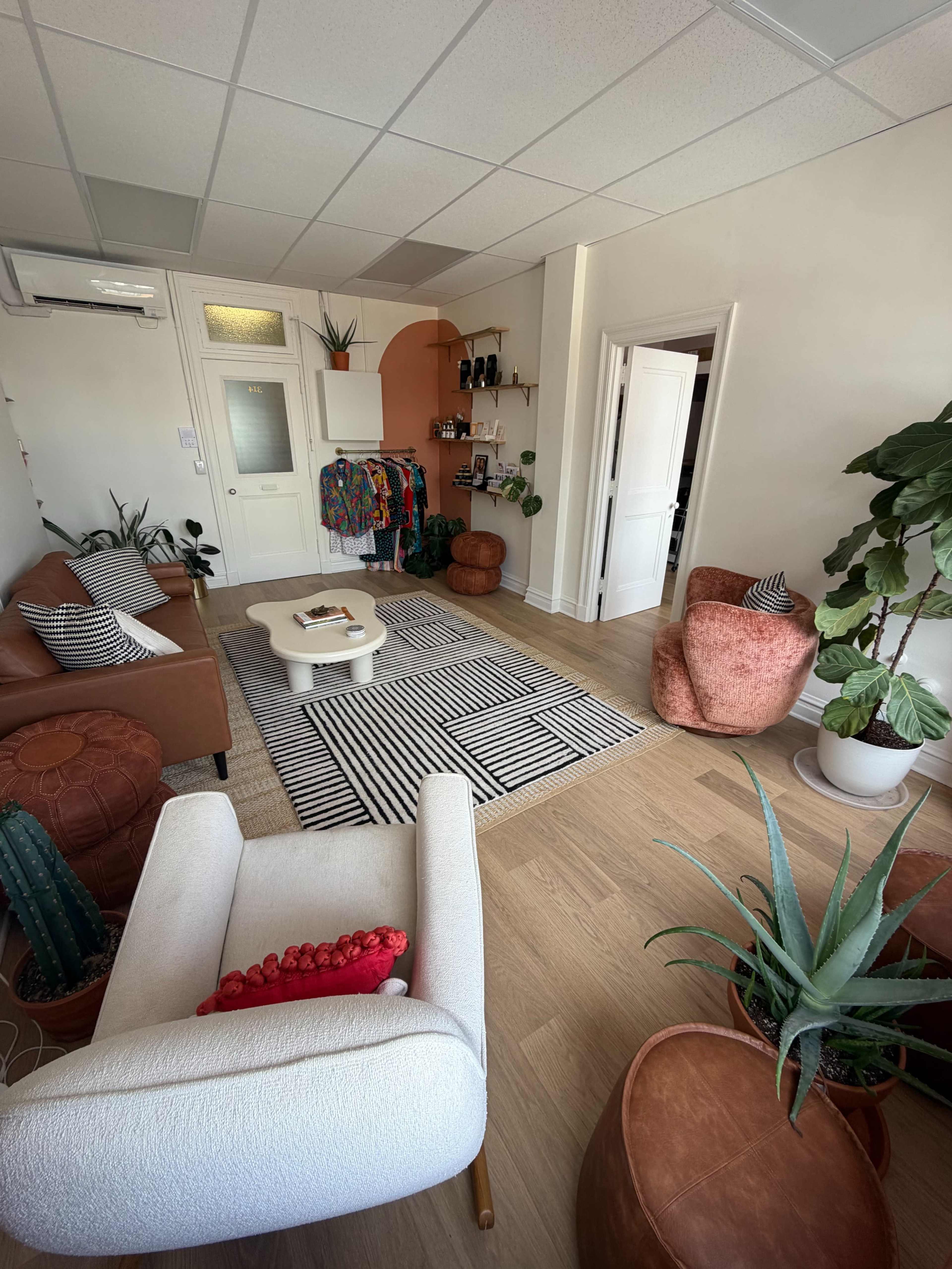 A cozy, well-lit interior space features a mix of seating options, a striped area rug, and several potted plants.