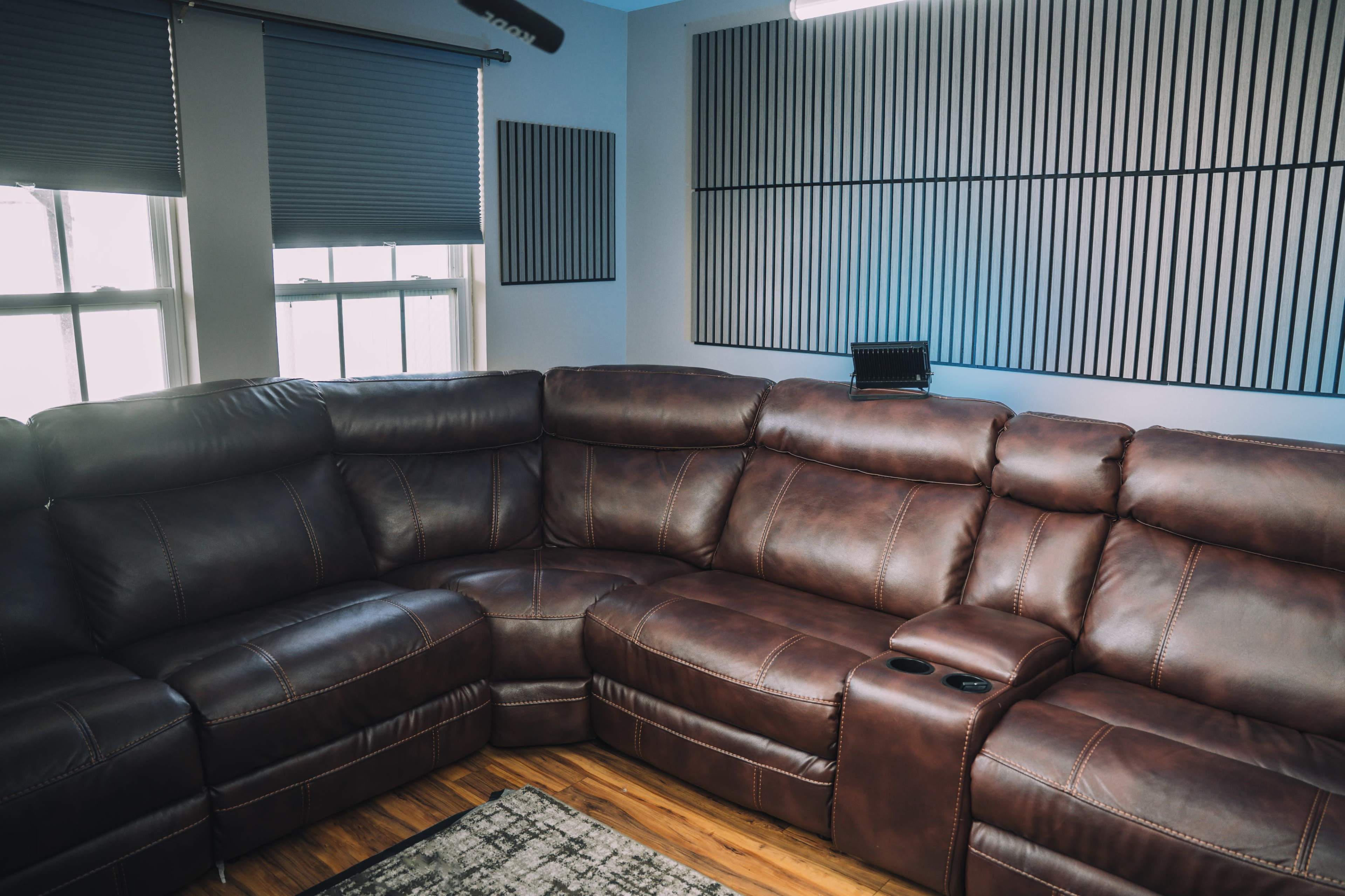 The image shows a brown leather sectional sofa in a room with light-colored walls and acoustic panels on the side.