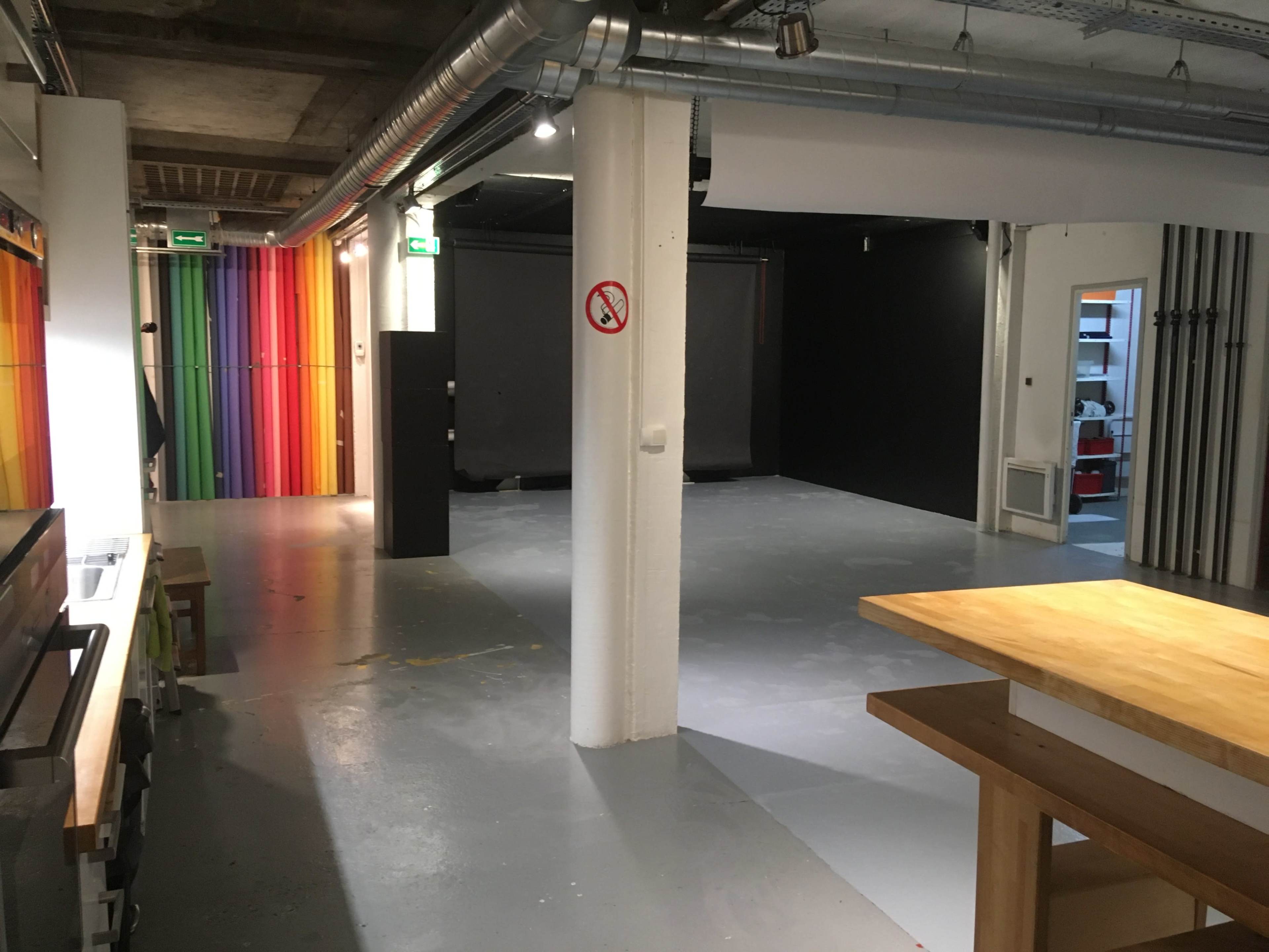 An empty studio space with a gray floor, white pillars, and colorful striped walls on one side.
