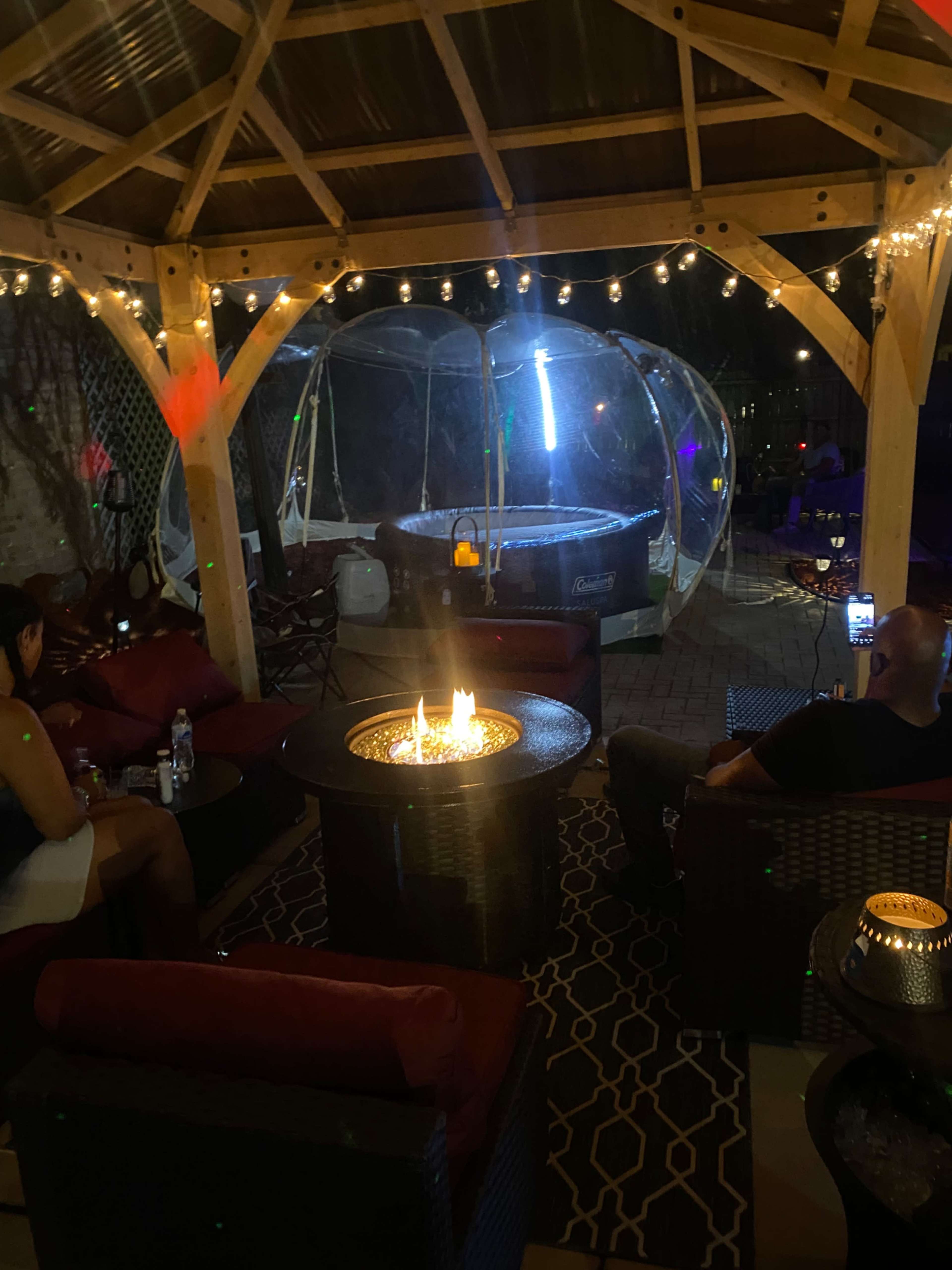 A covered outdoor seating area with a fire pit, string lights, and a nearby inflatable hot tub.
