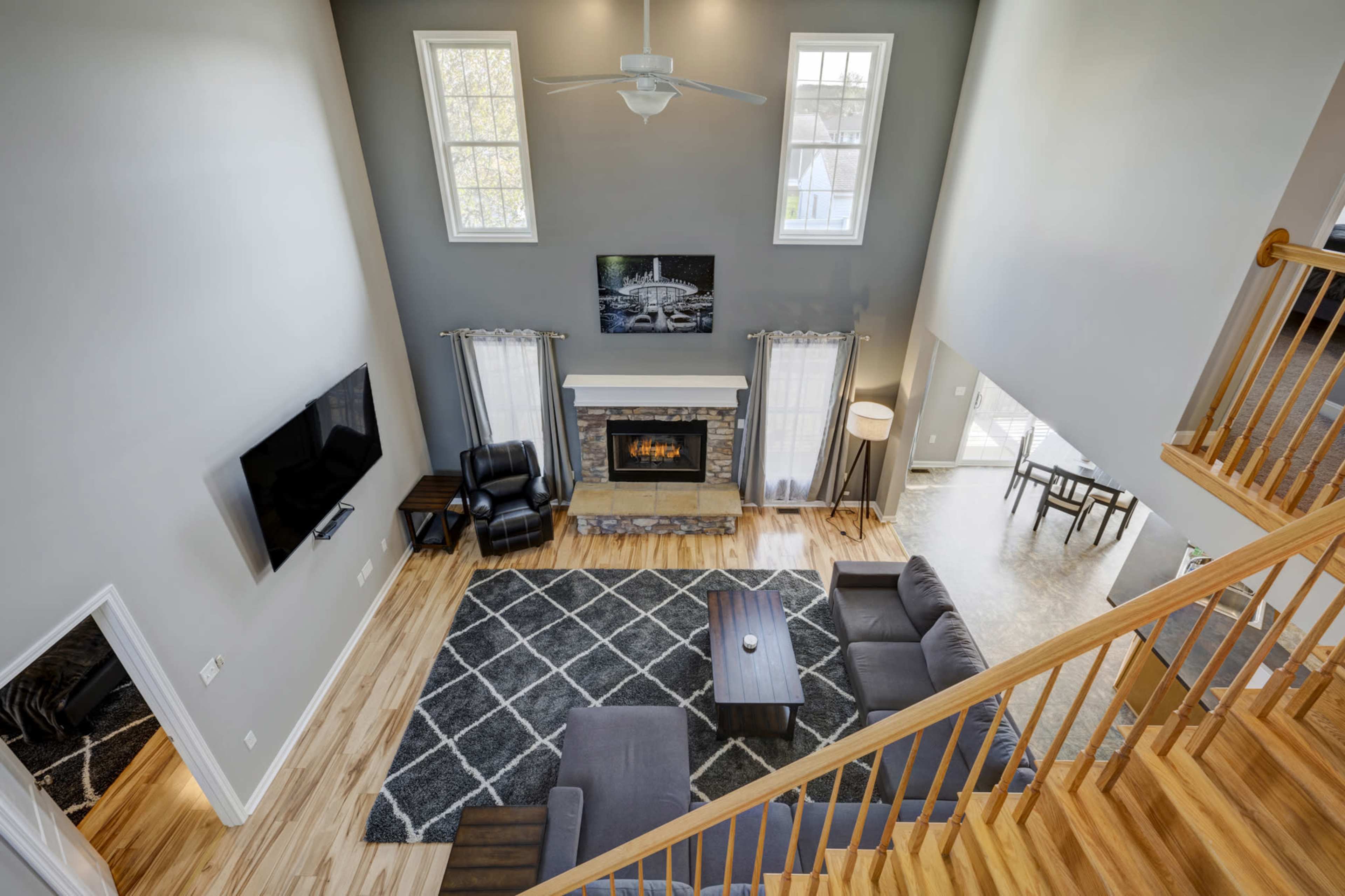 A spacious living room with a large window, a stone fireplace, modern furniture, and a ceiling fan.