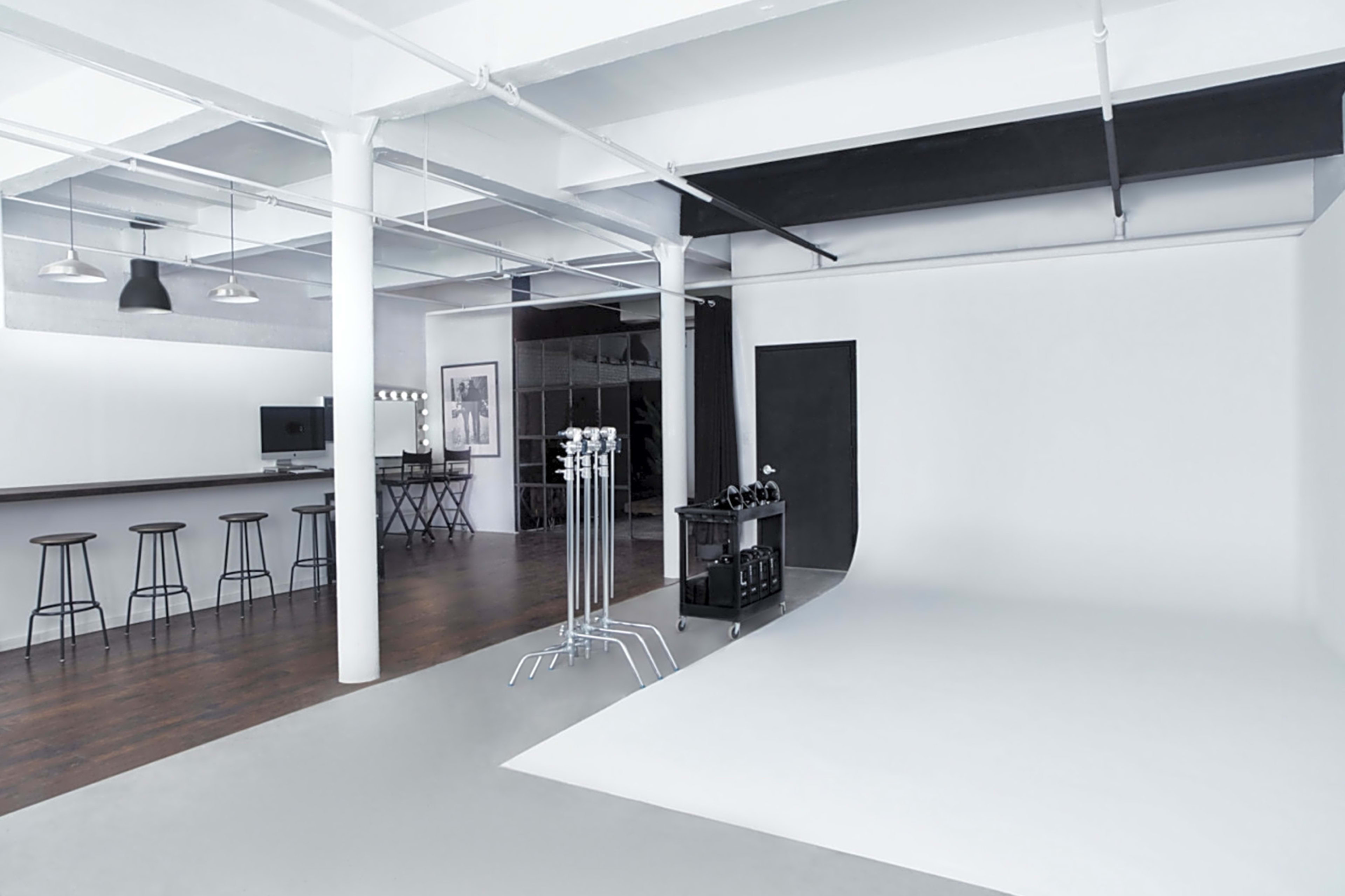 A spacious studio with a bar area, tall stools, and a plain white backdrop for photography.