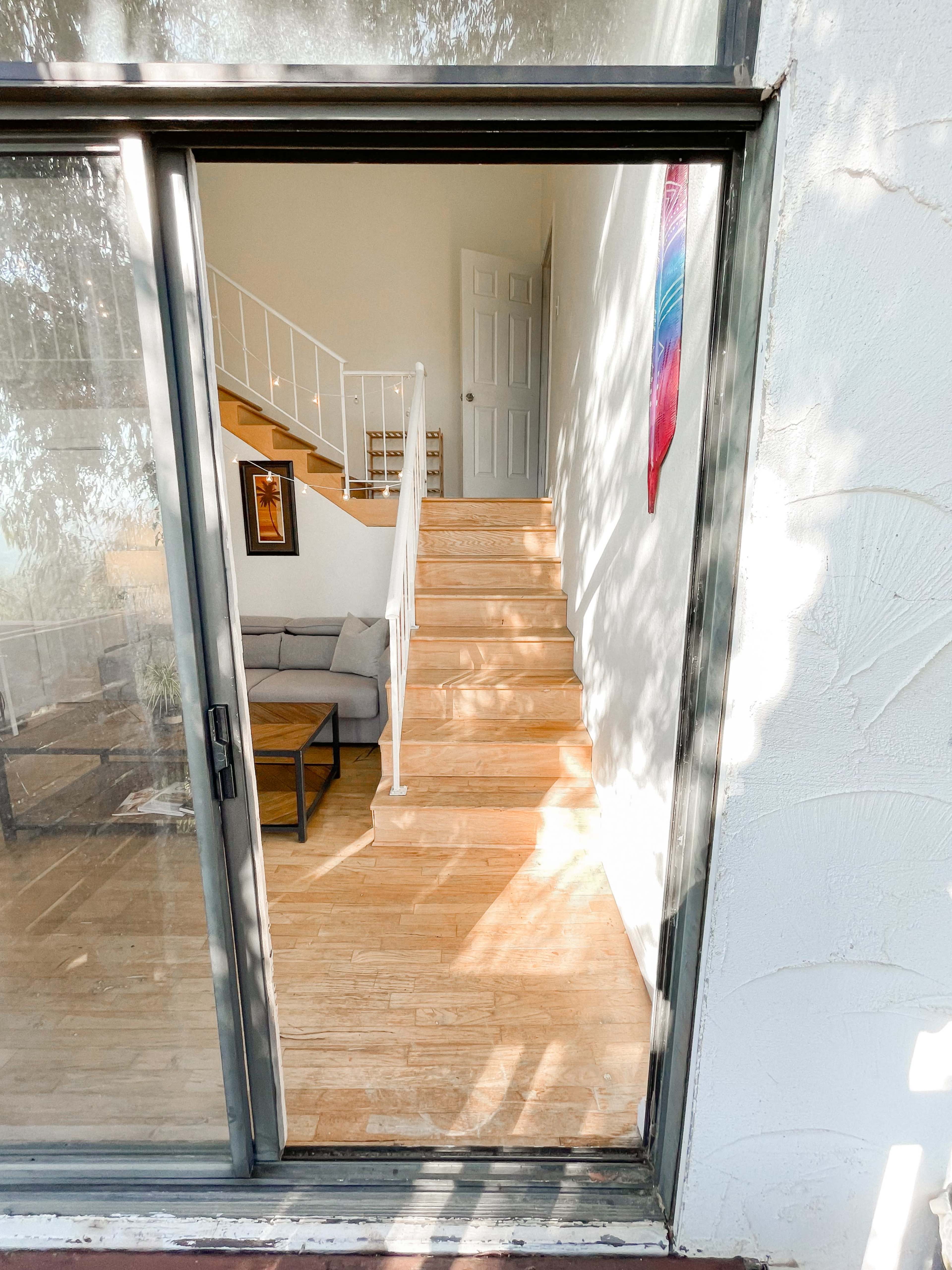 A glass door opens to a spacious room with a staircase leading to a second floor.