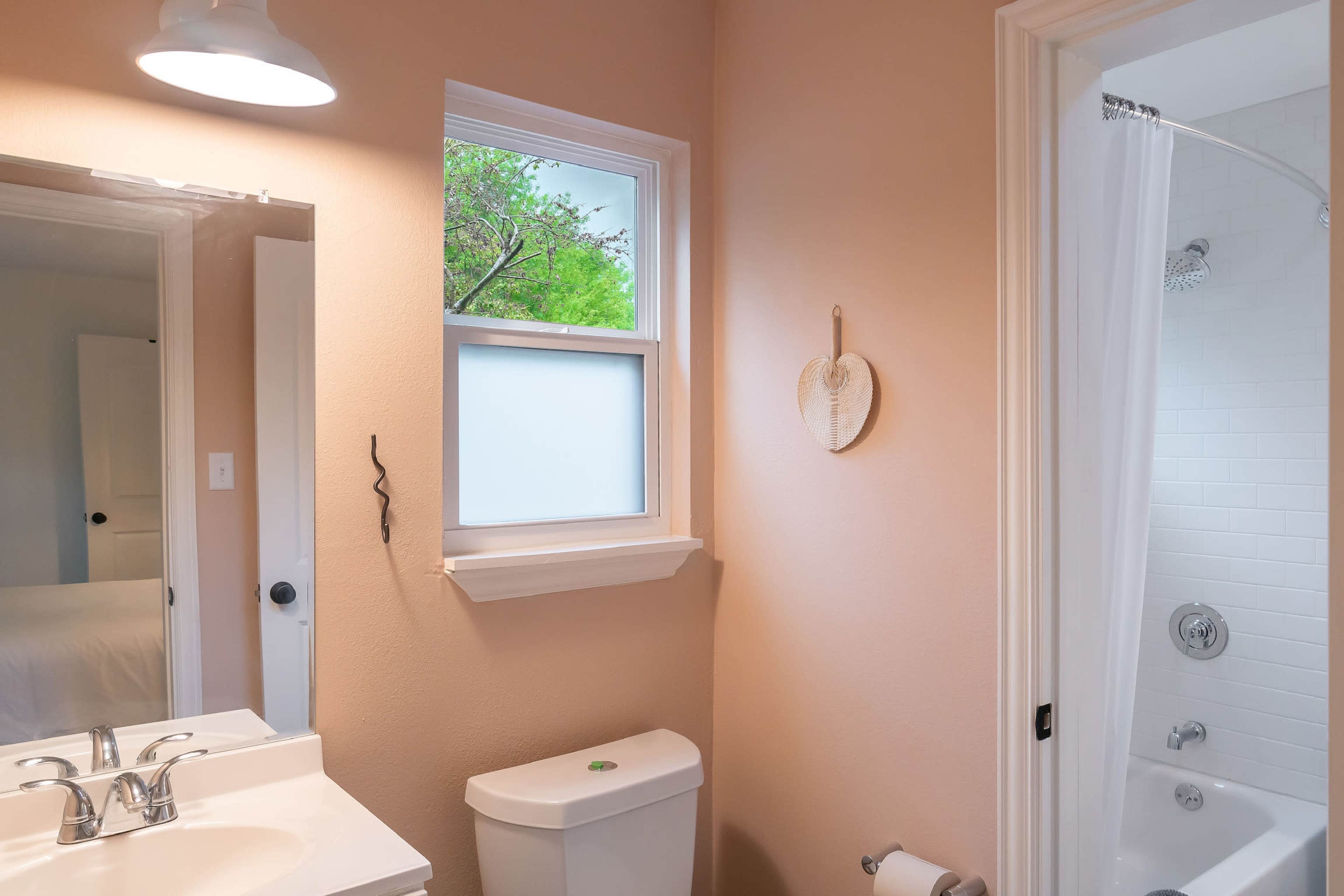 A bathroom features a double sink vanity, a toilet, and a glass shower, with a window allowing natural light.