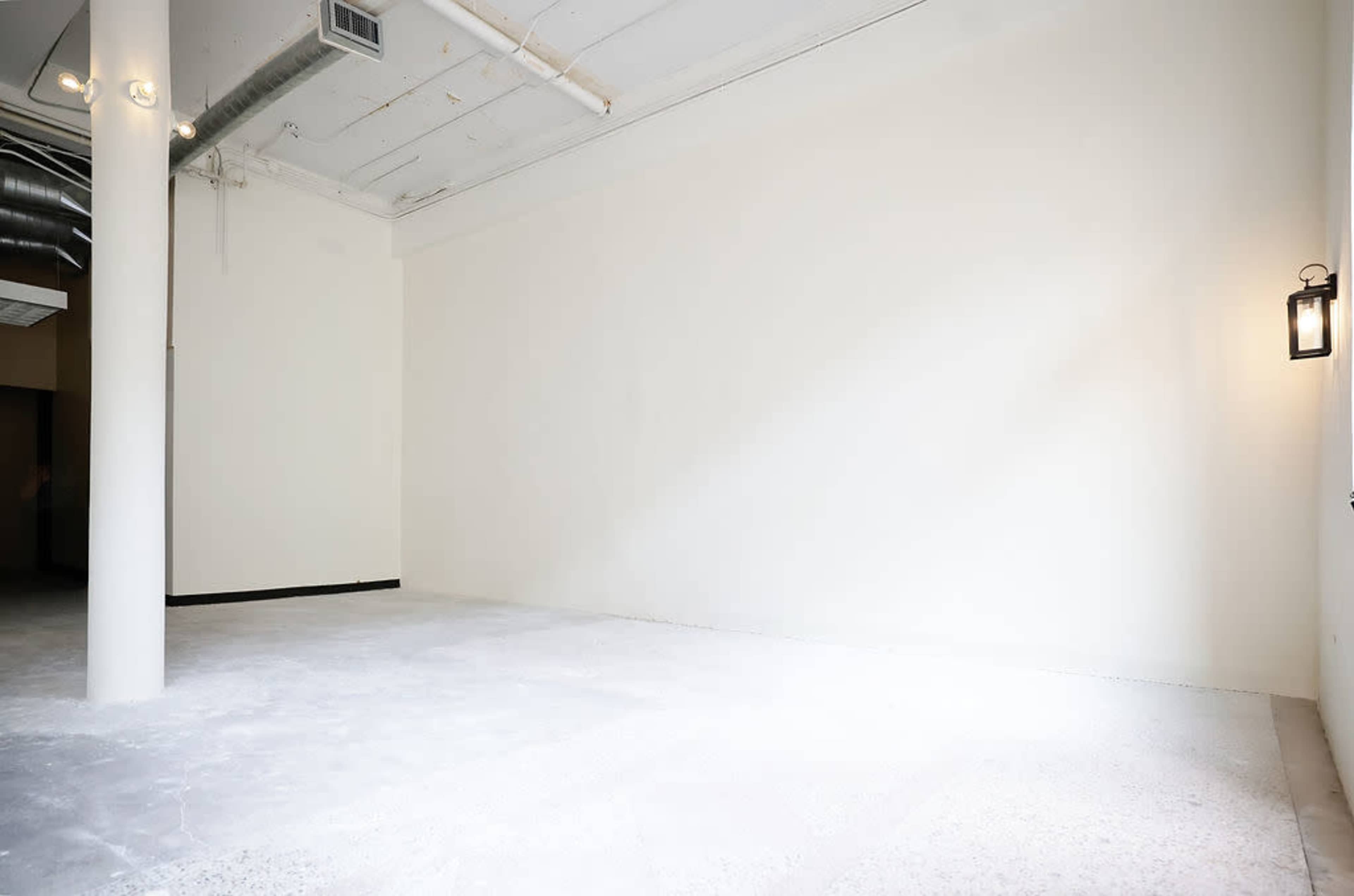 The image shows an empty room with white walls and a bare concrete floor.