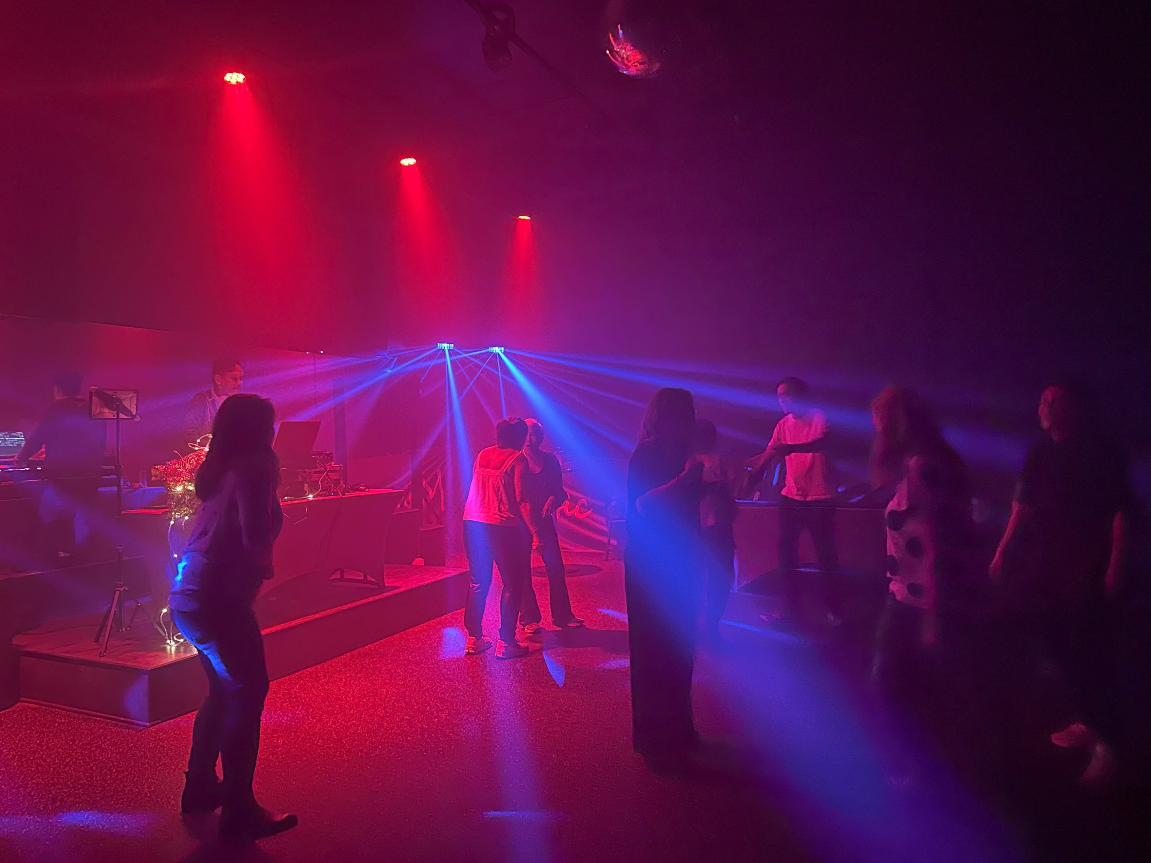 A group of people dance under colored lights in a nightclub setting.