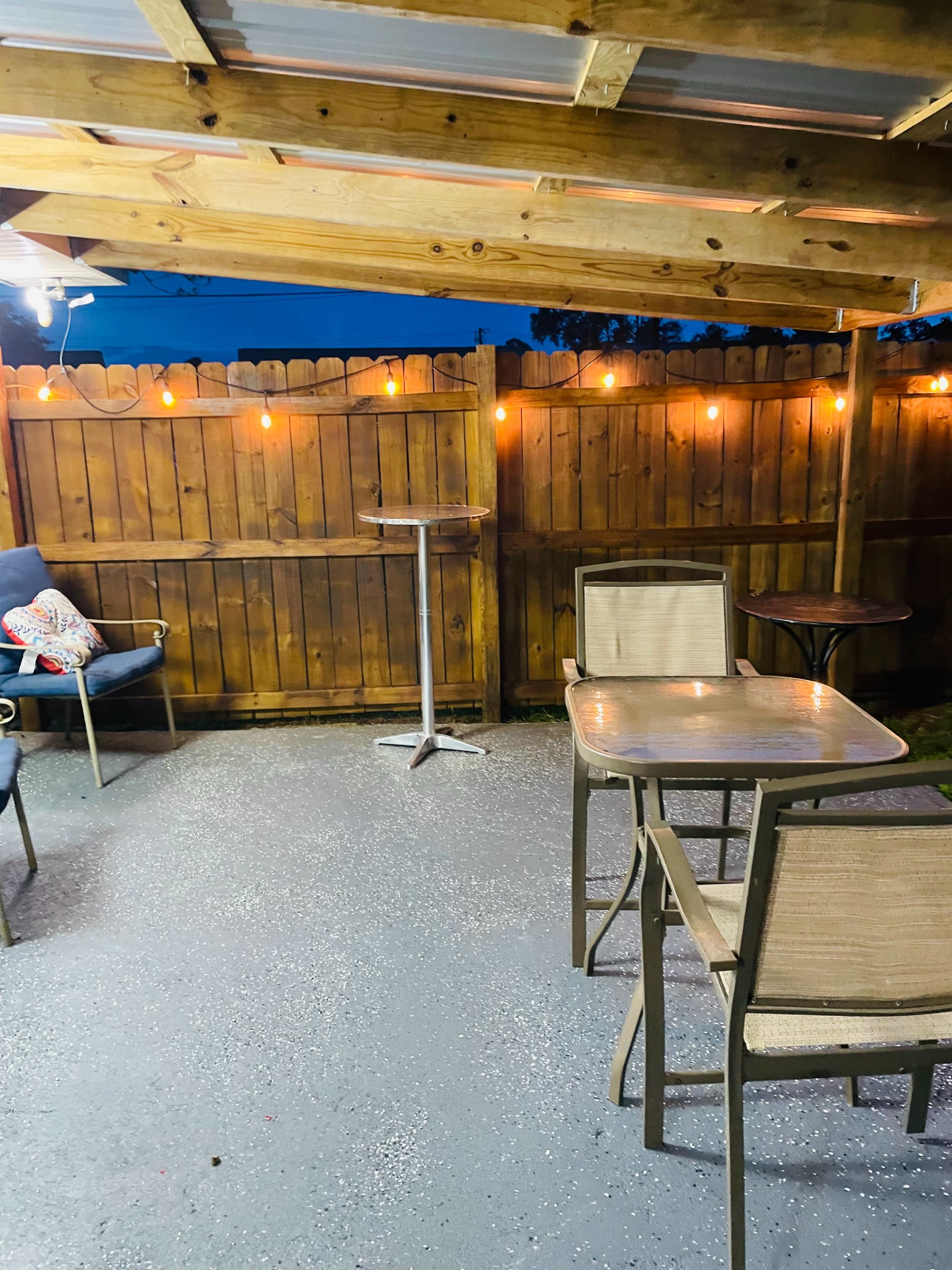 A patio area with a wooden fence, a table and chairs, and string lights illuminating the space.