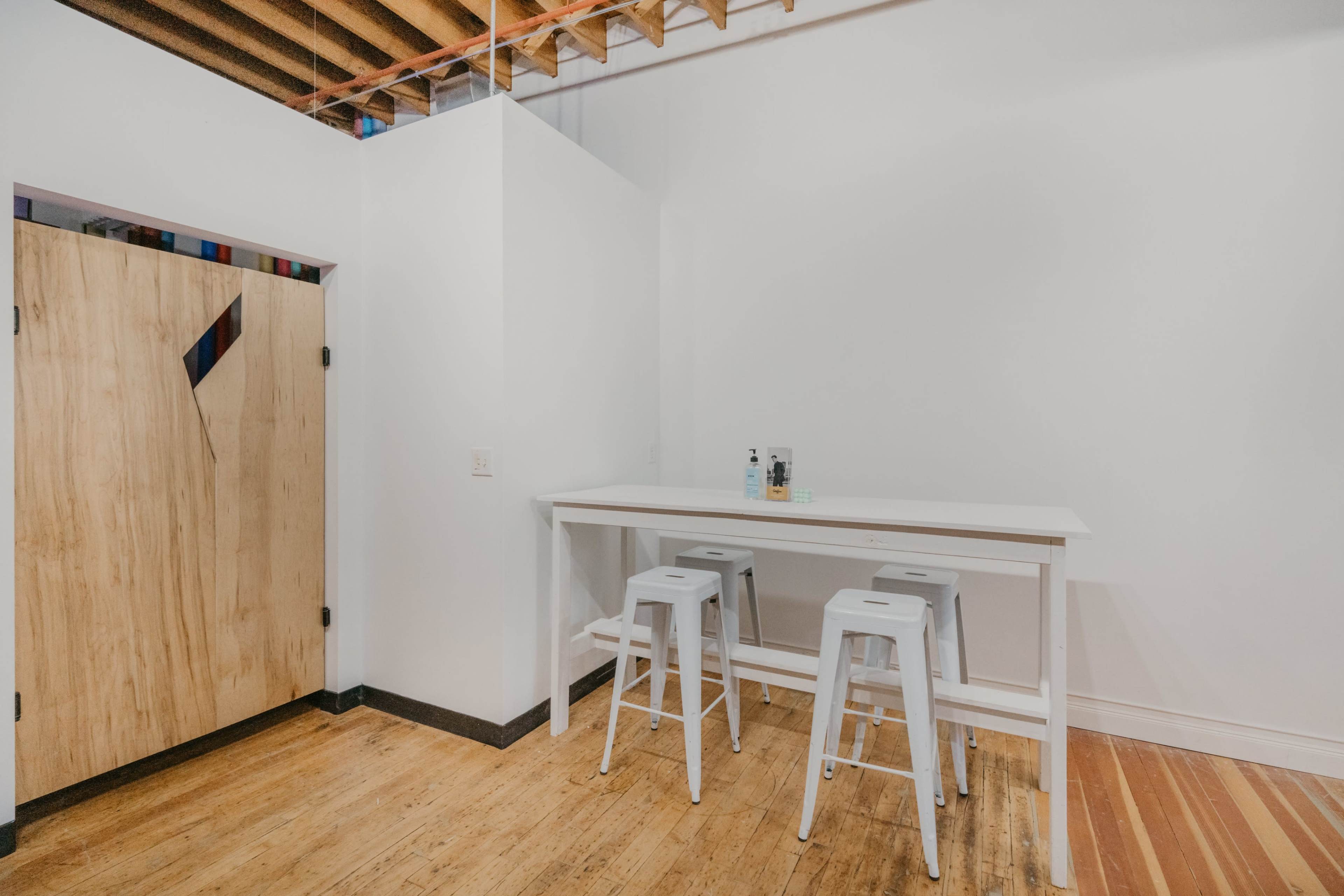 A minimalist dining area features a white table surrounded by metal stools next to a wooden door with a diagonal design.