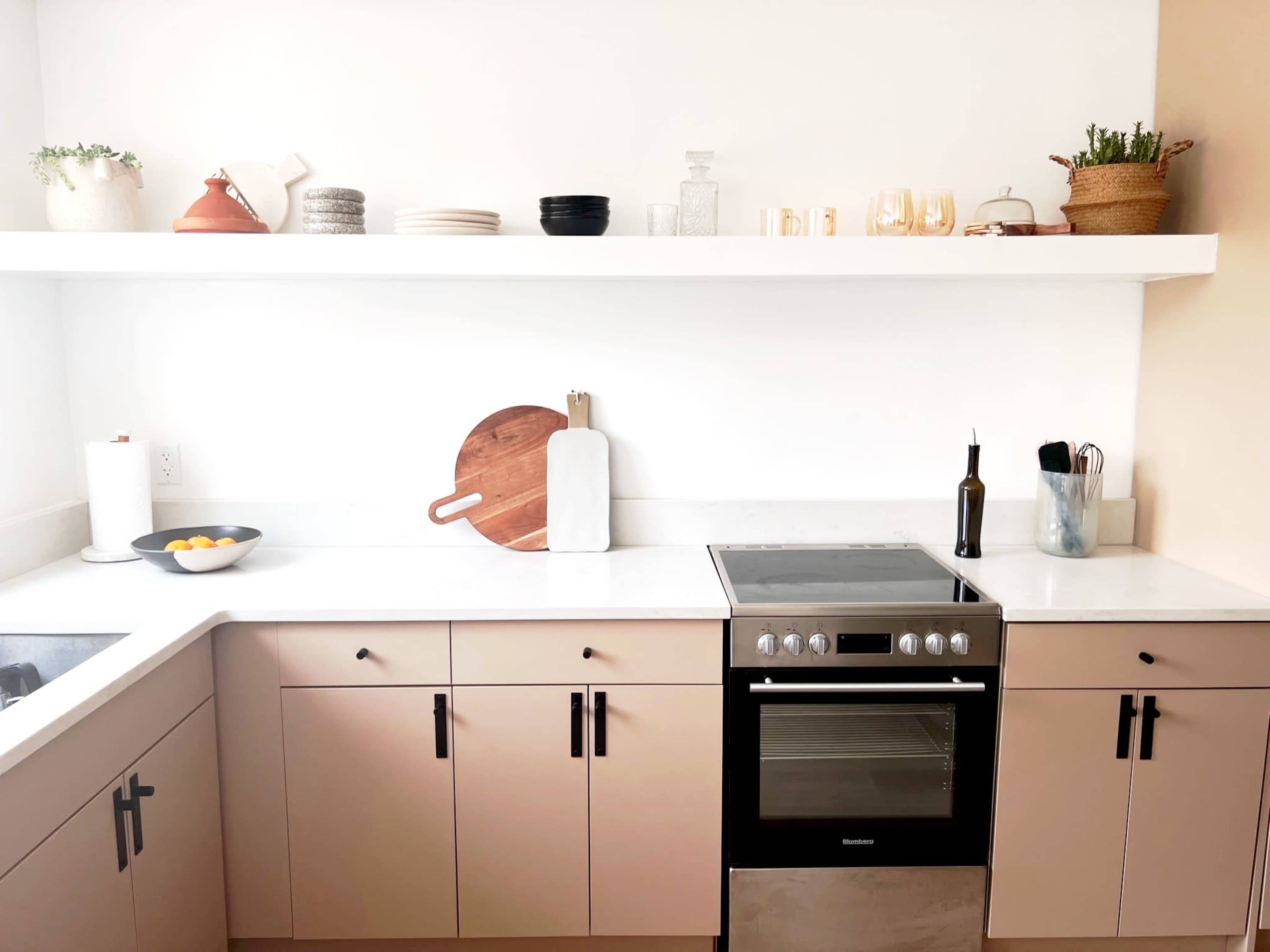 A modern kitchen with a black oven, light-colored cabinetry, a countertop, and shelves displaying various dishes and decor.