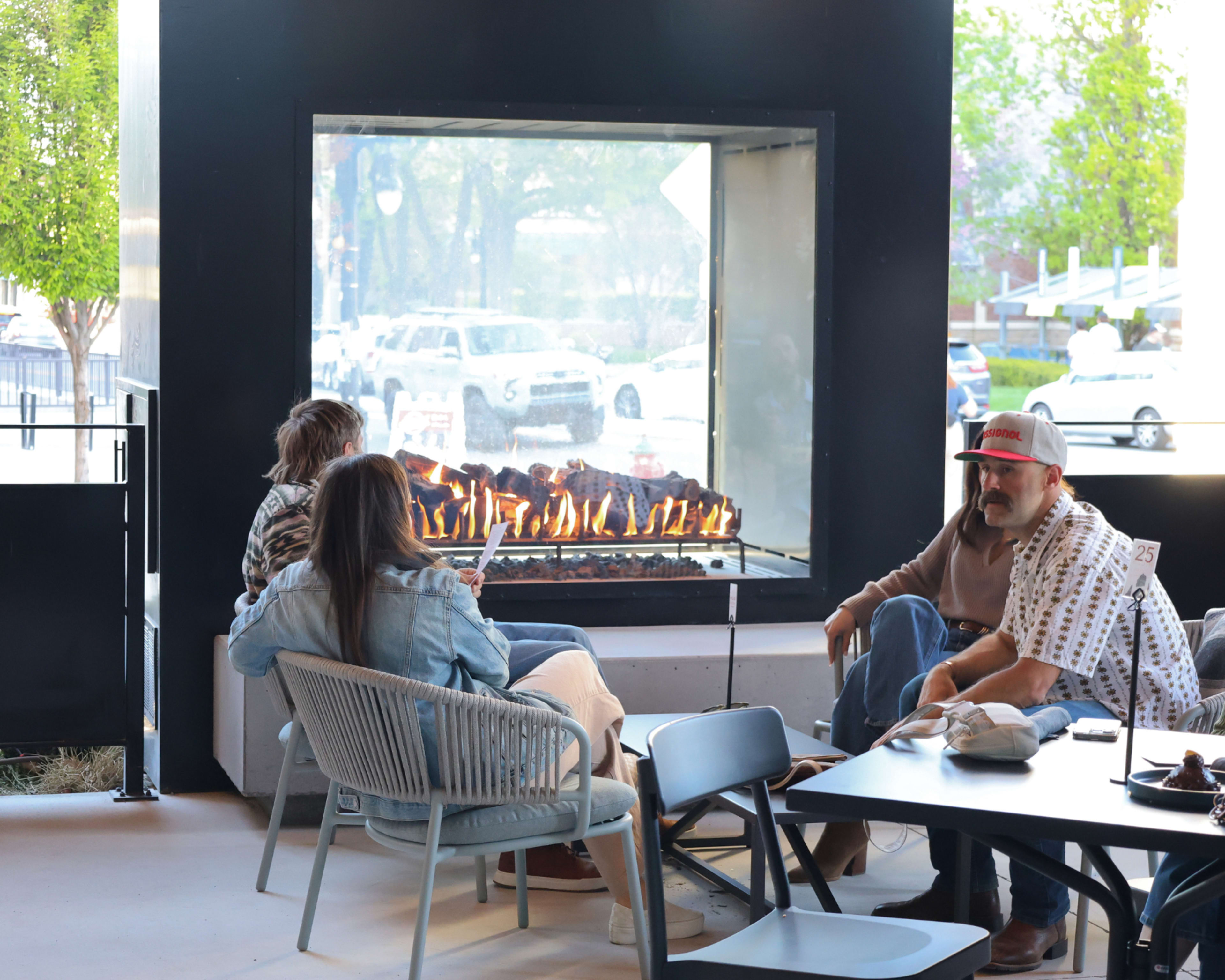 People are seated around a modern fireplace in a seating area with outdoor views.