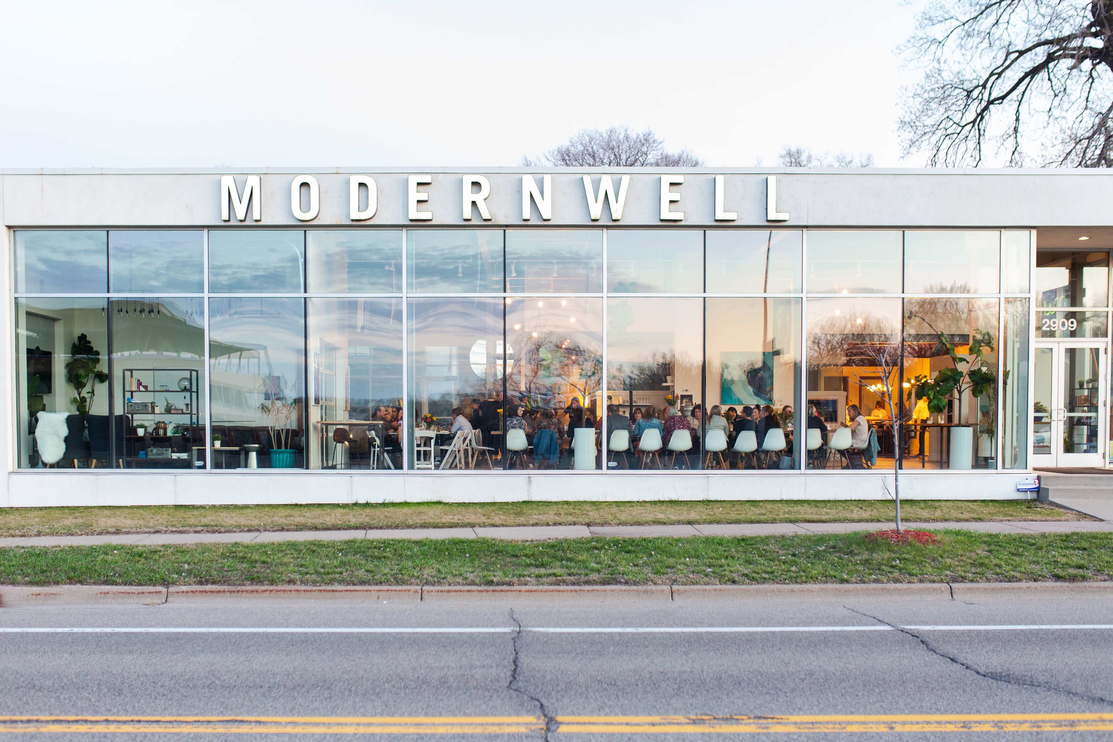 The image shows a modern storefront with large windows displaying a contemporary interior and seating area.
