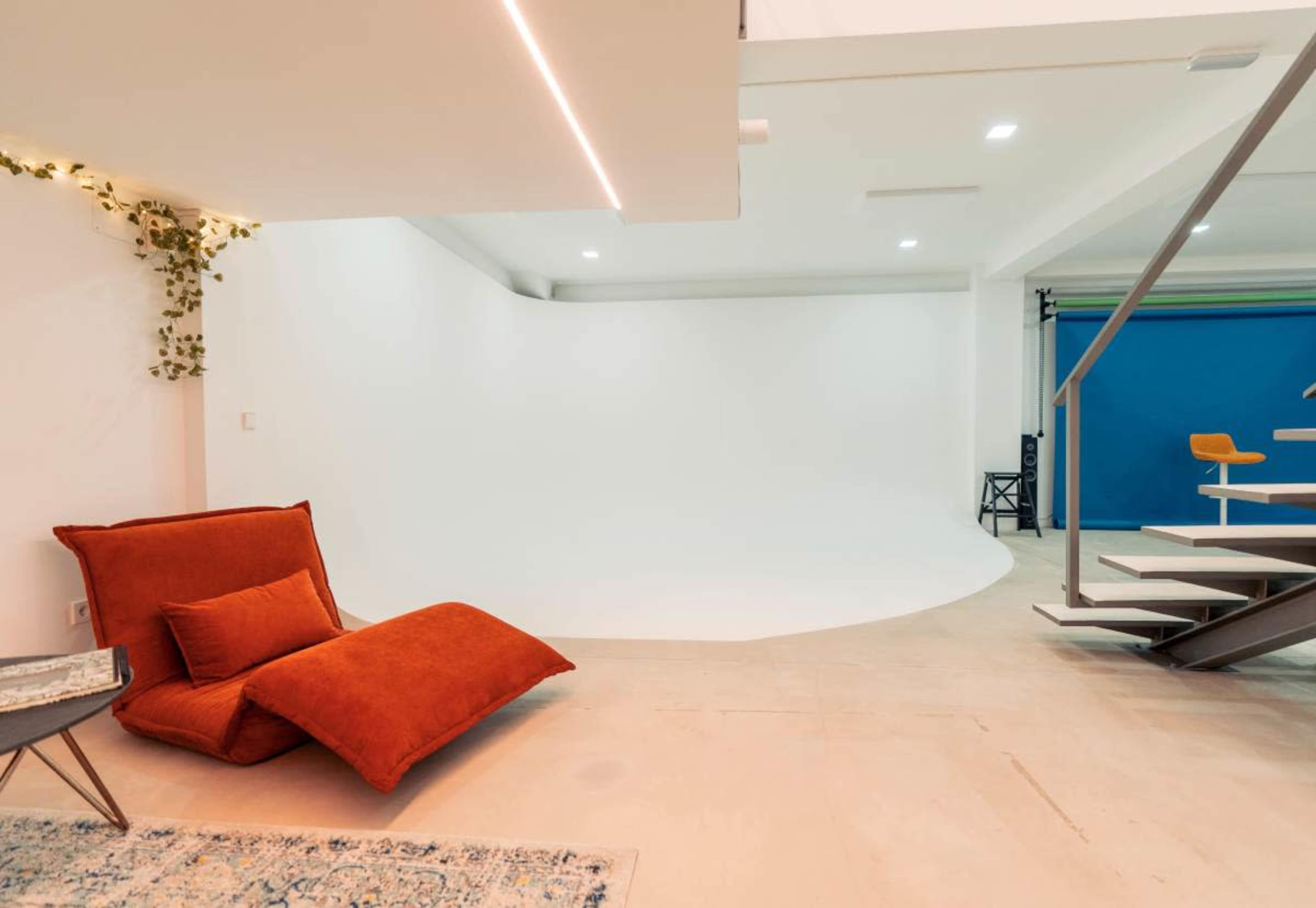 The image shows a modern studio space featuring a large curved backdrop, a red seating area, and a blue backdrop on the left side.