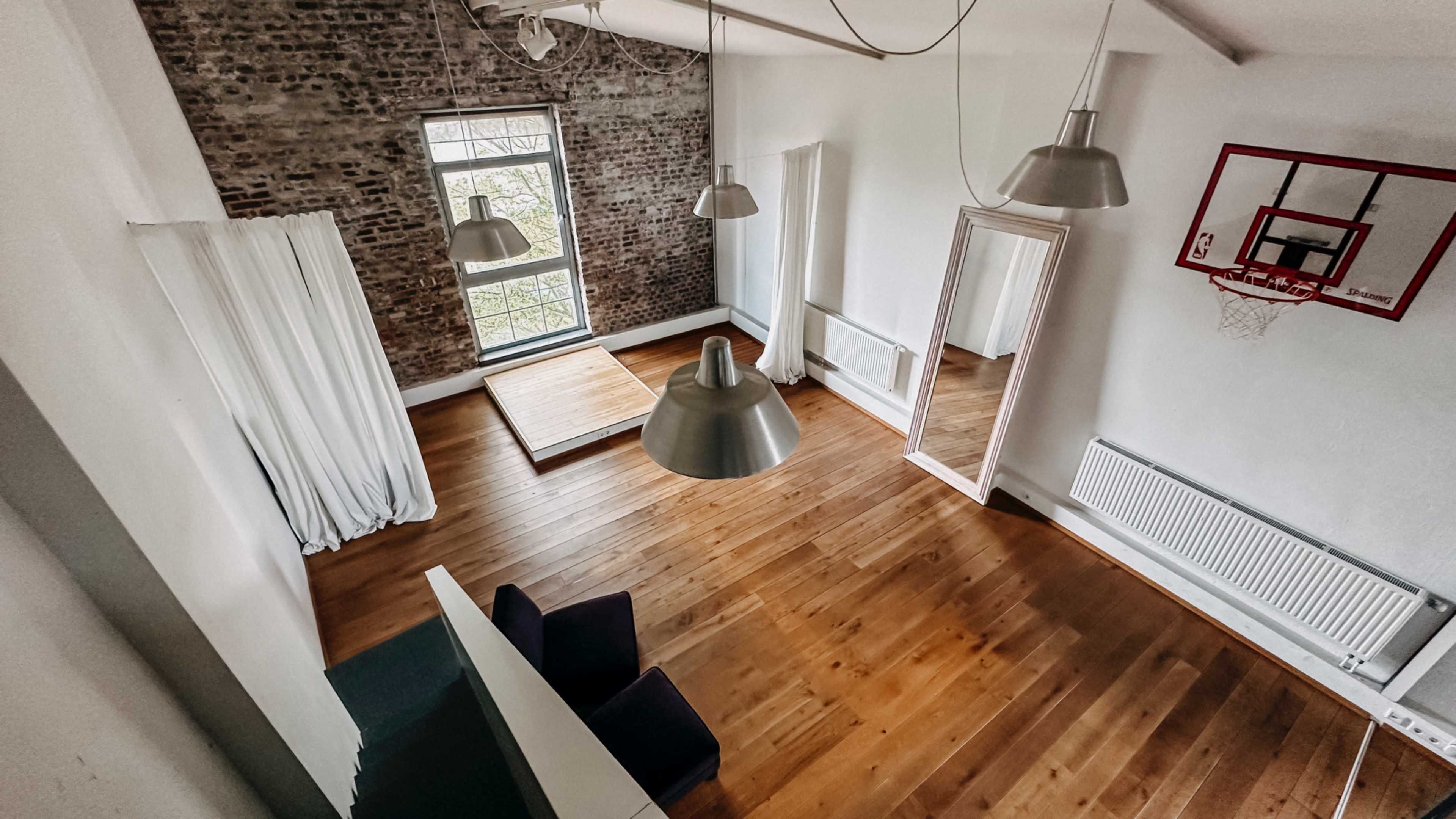 The image shows a spacious room with hardwood flooring, a large mirror, and a basketball hoop mounted on the wall.