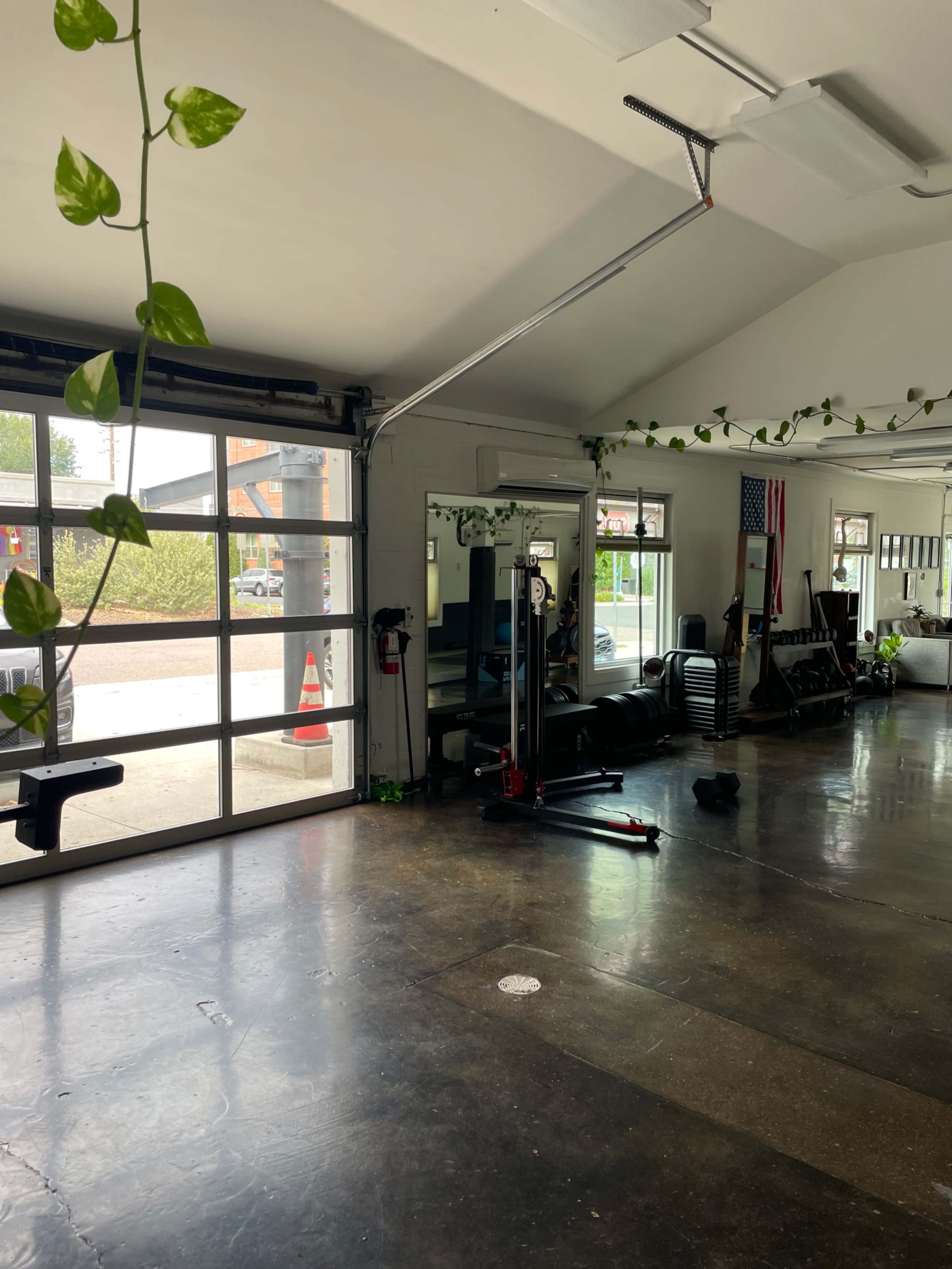 The image shows a spacious gym interior with various workout equipment and large glass doors allowing natural light to enter.