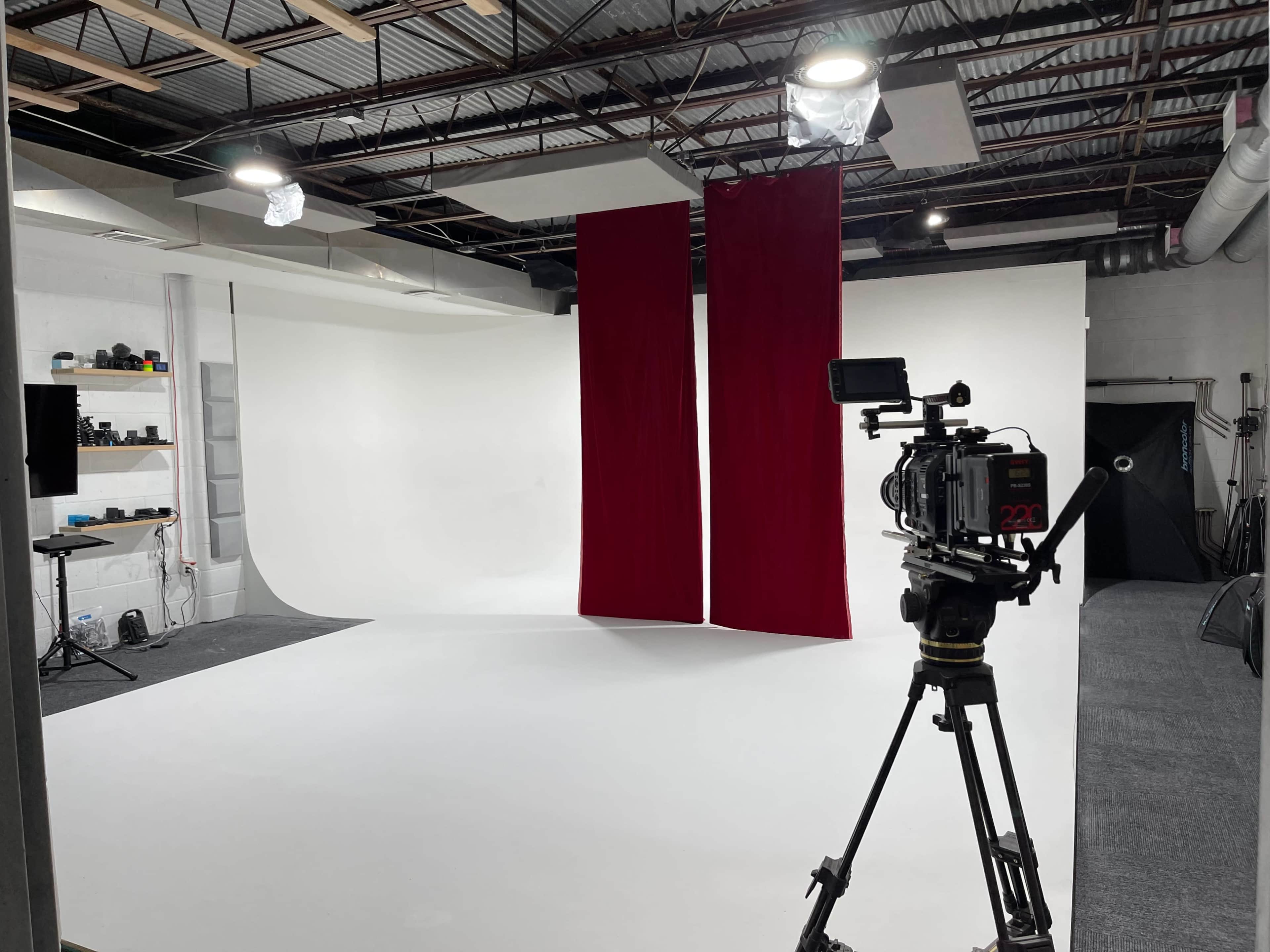 A photography studio with a white backdrop, two red curtains, and a camera on a tripod positioned in the foreground.