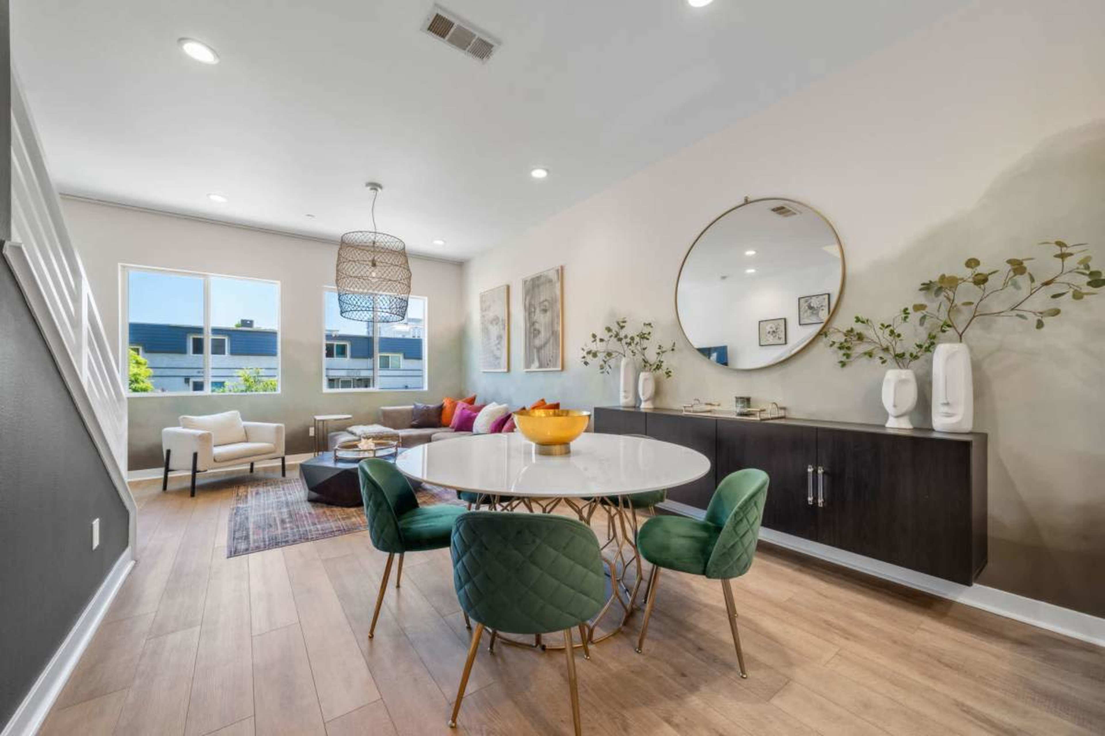 A modern dining area features a round table with green chairs, a large mirror, and a cozy seating arrangement in a well-lit space.