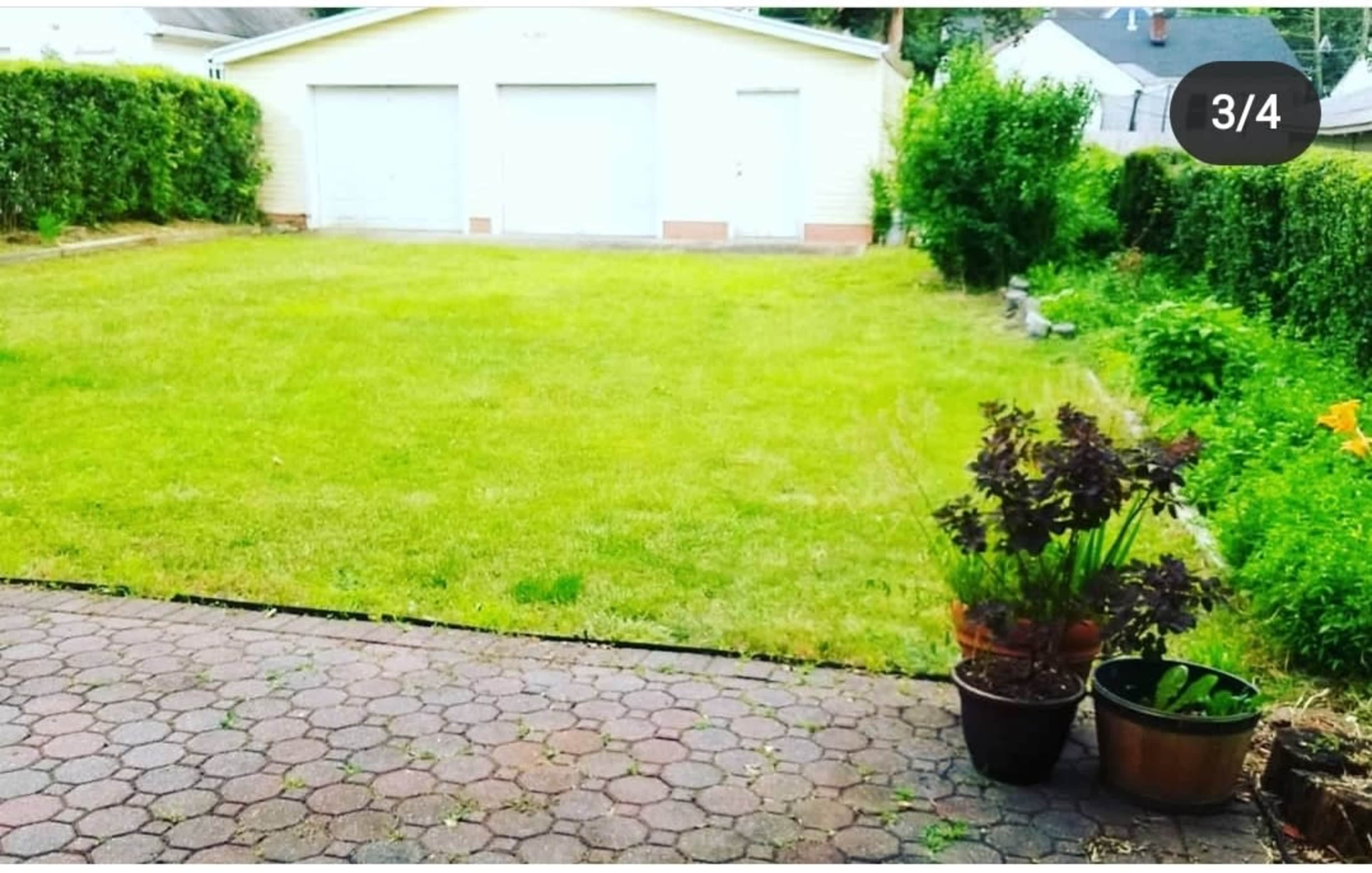 A grassy backyard with a gravel patio, two flower pots, and a view of a garage in the background.