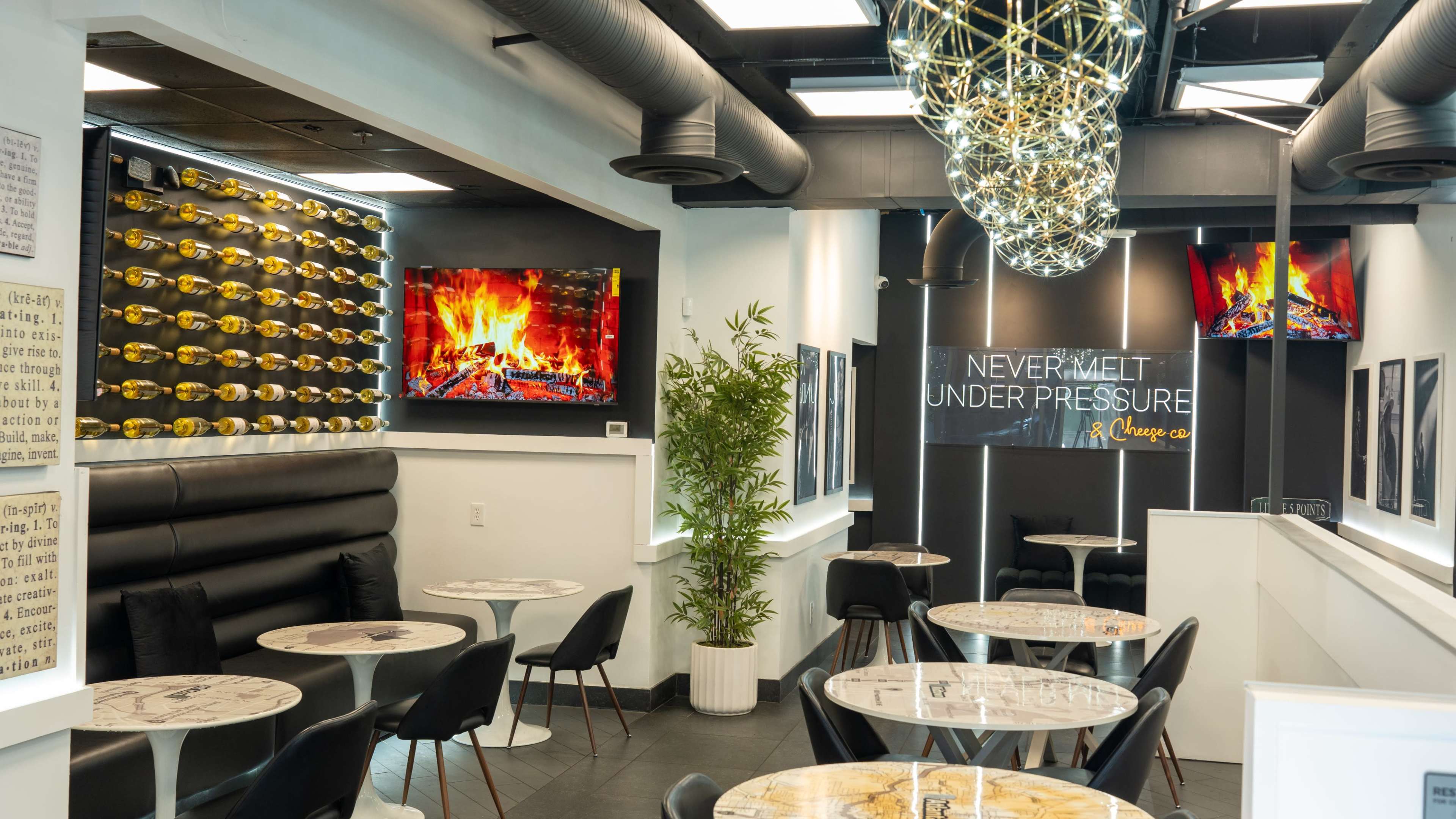 The image shows a modern café with contemporary decor, featuring black seating, marble tables, and a wall adorned with wine bottles and digital artwork.
