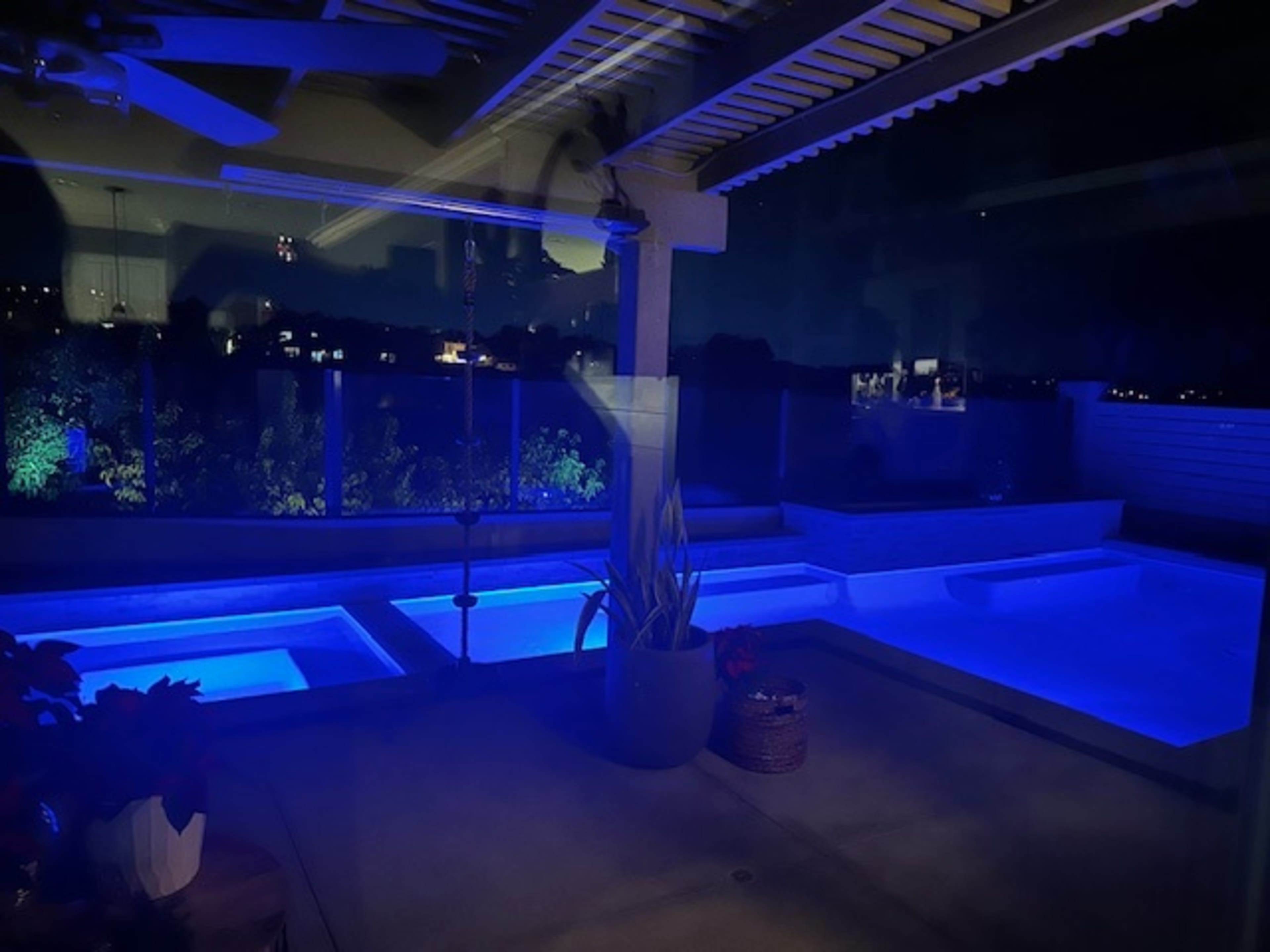 A modern outdoor pool area illuminated by blue lights at night.