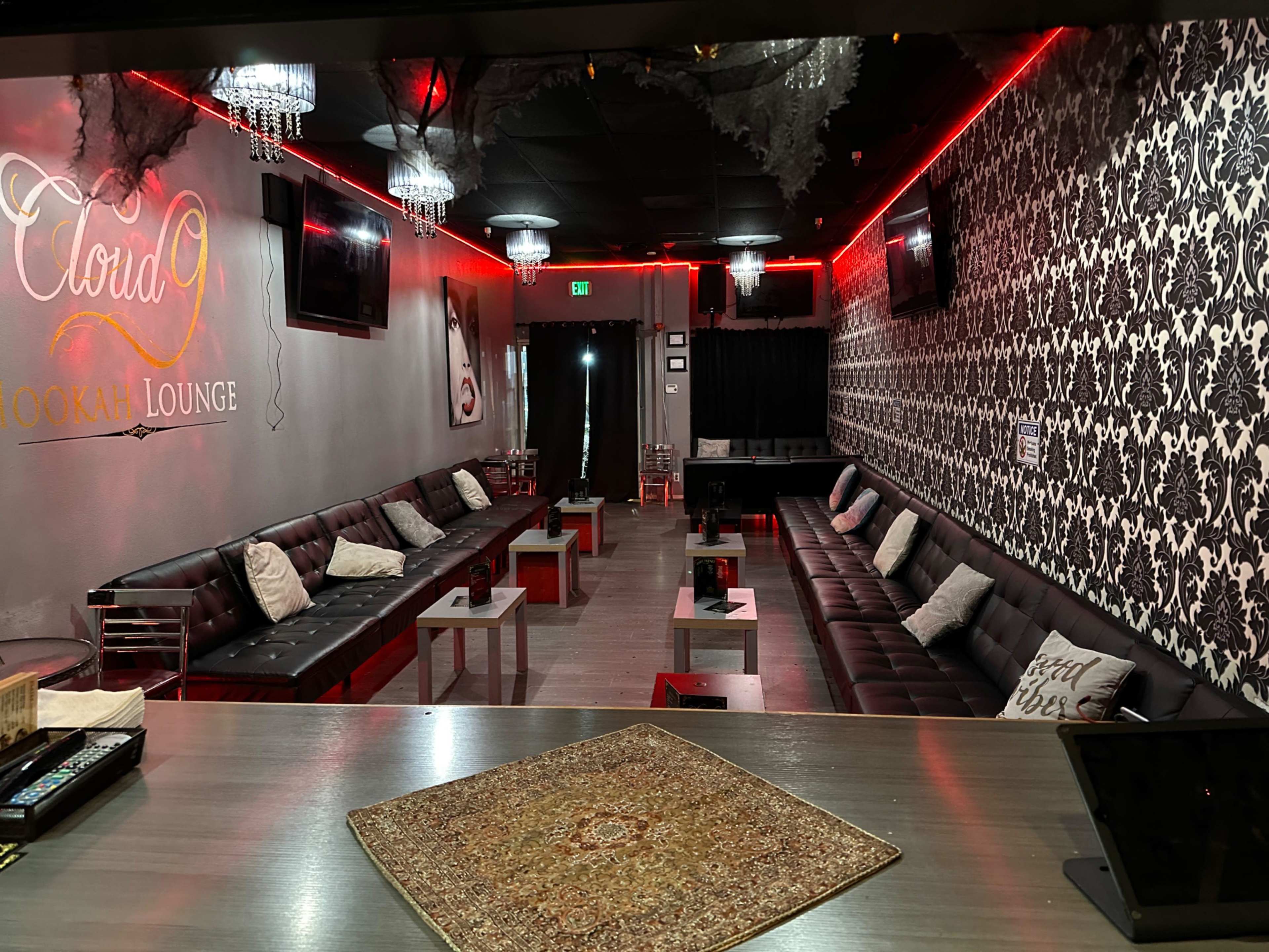 The image shows a stylish lounge area with dark leather seating, decorative chandeliers, and a modern black-and-white patterned wall.