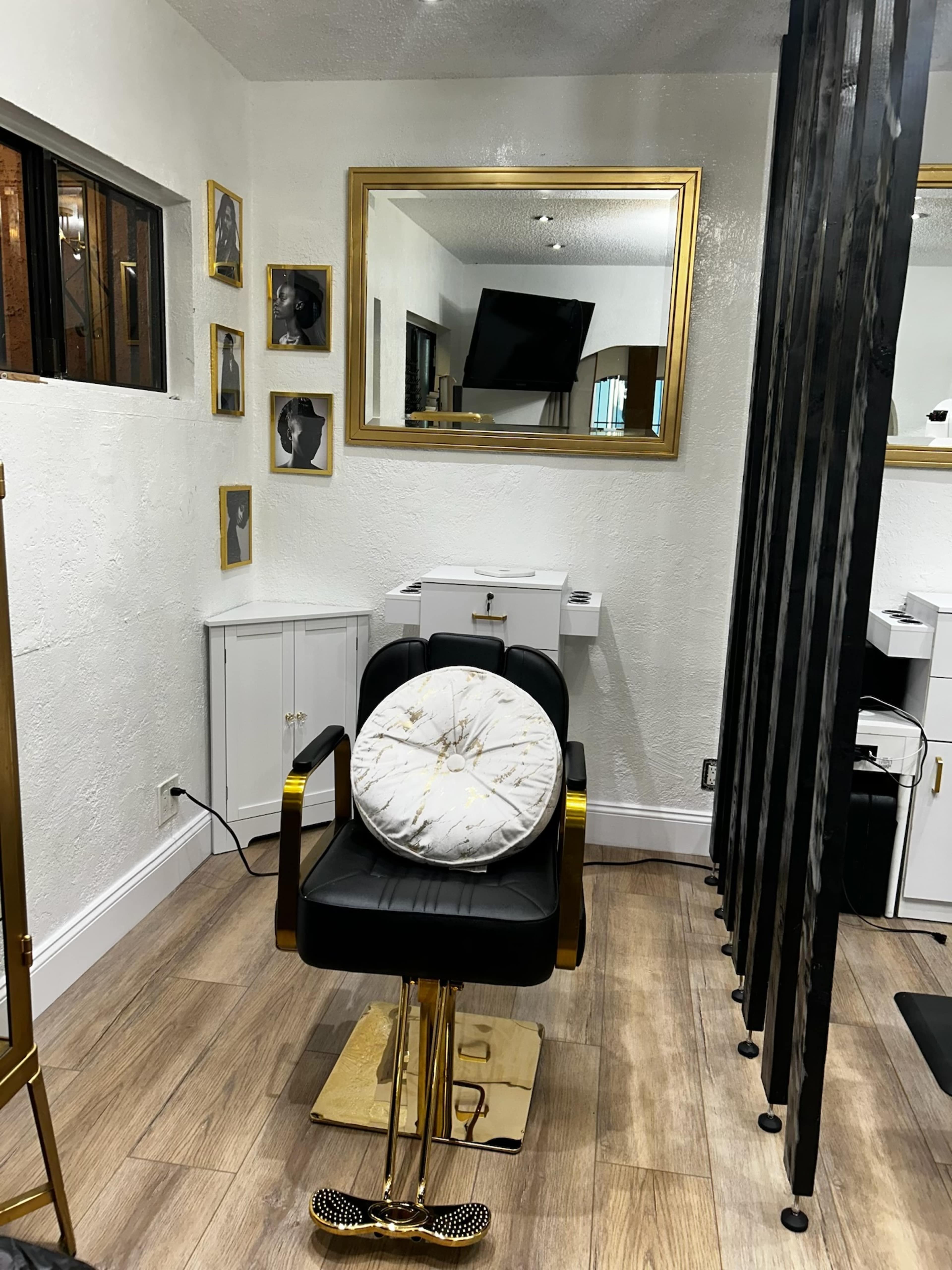 The image shows a modern hair salon interior featuring a black salon chair, a large gold-framed mirror, and partitions made of vertical black strips.
