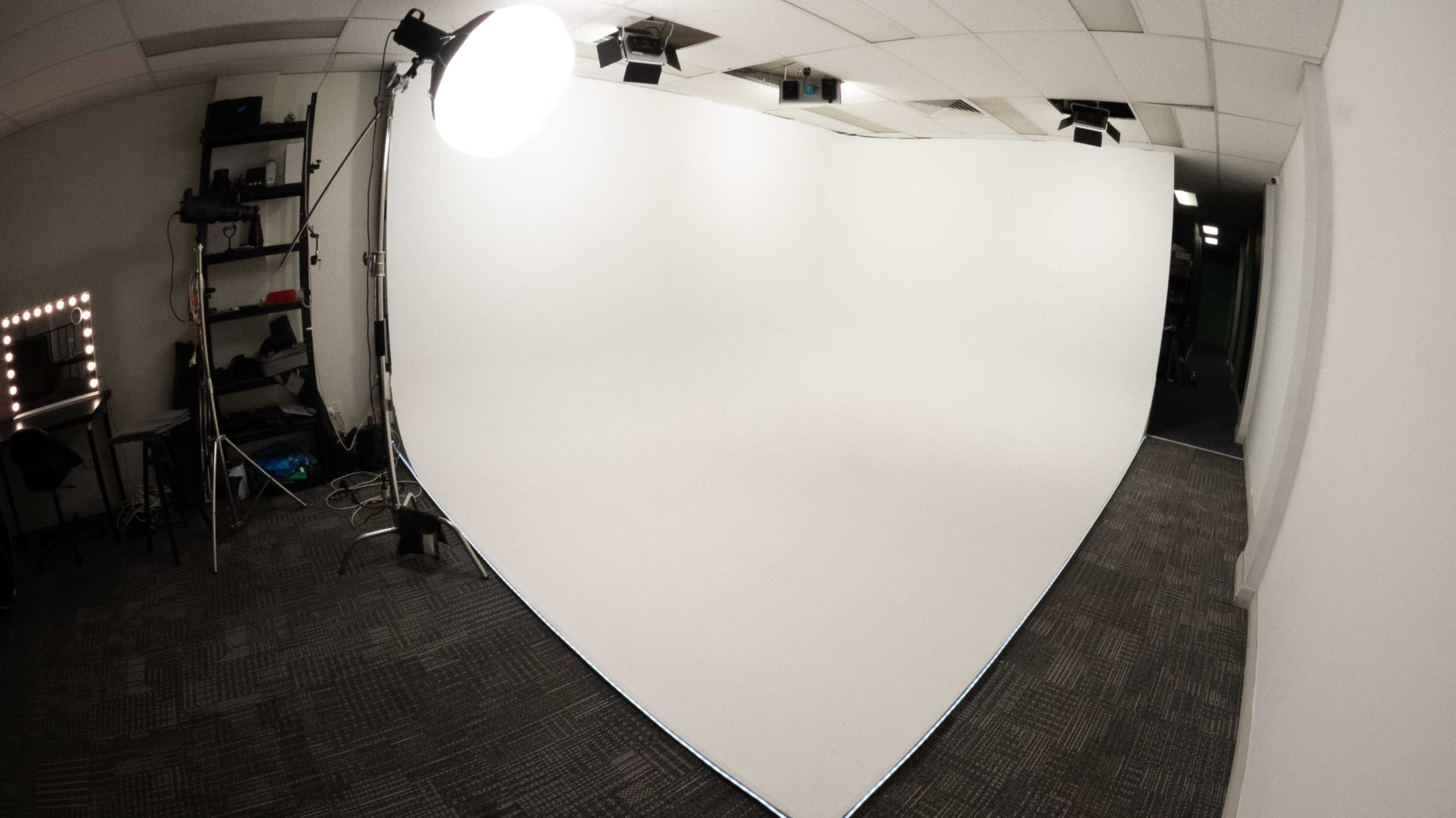 The image shows a photography studio with a seamless white backdrop and professional lighting equipment.