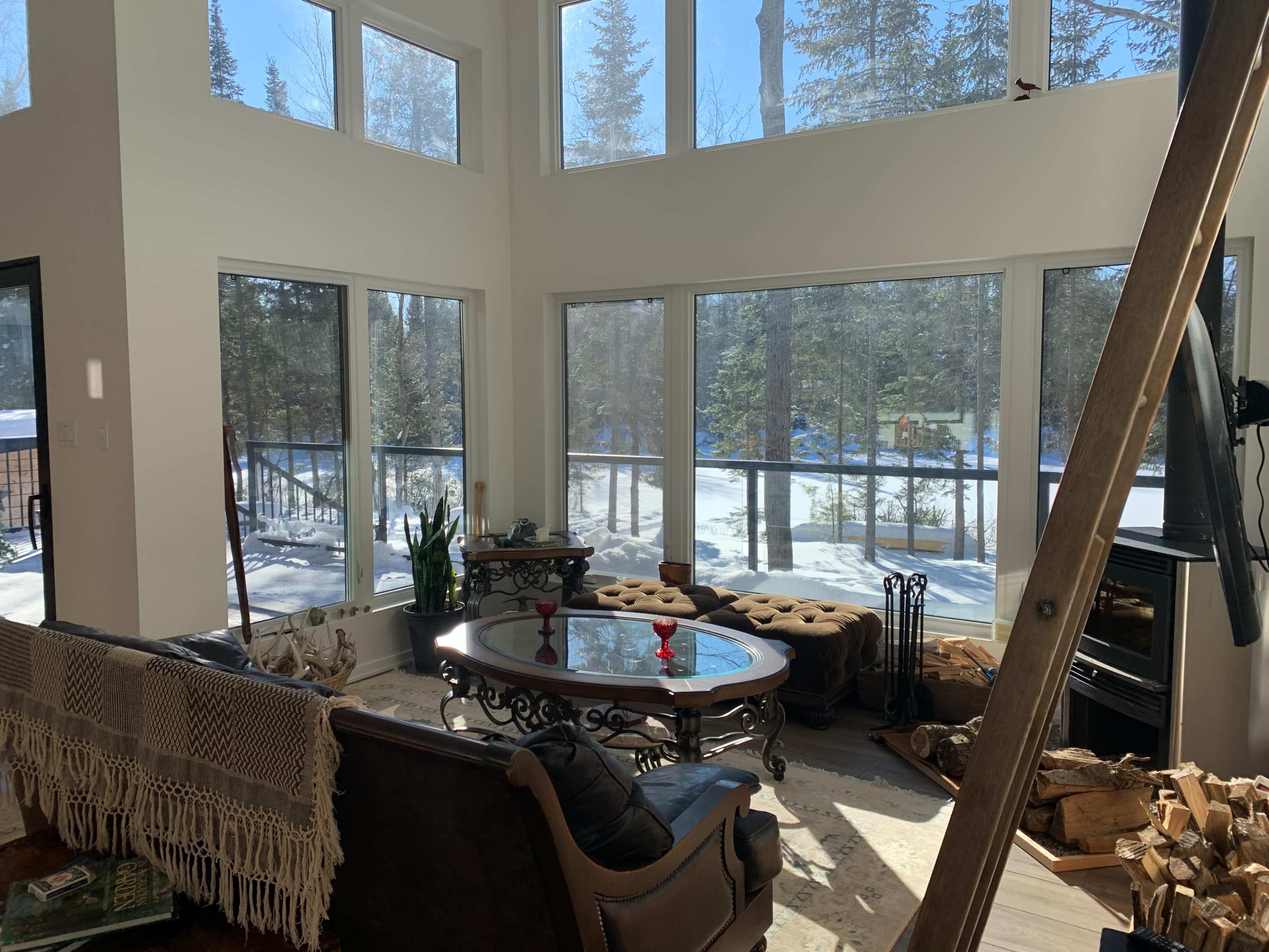 A spacious living room with large windows overlooks a snowy landscape, featuring a round table, upholstered seating, and a fireplace.