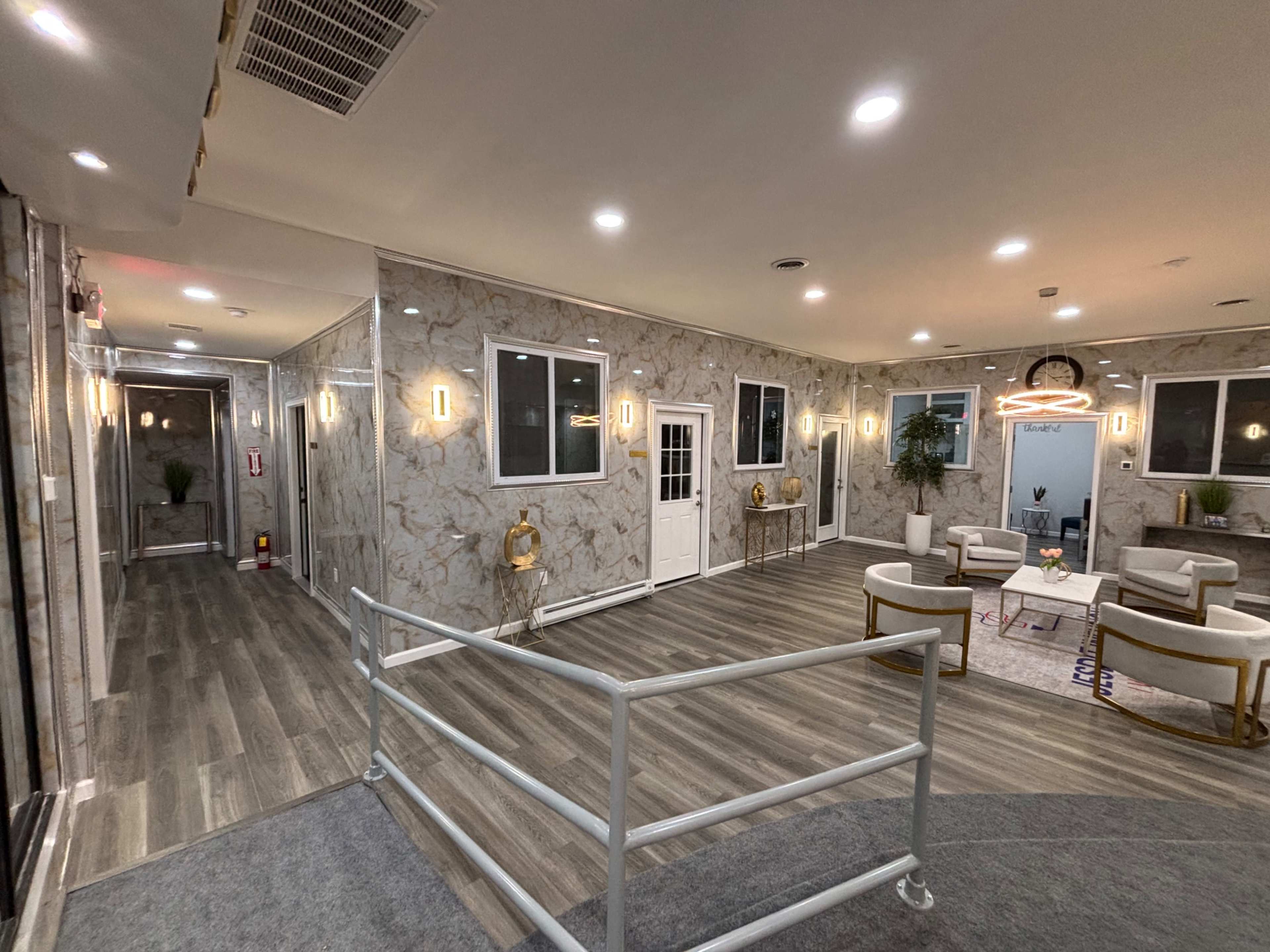 The image shows a modern indoor lobby with marble walls, a wooden floor, and seating areas, featuring large windows and decorative lighting.
