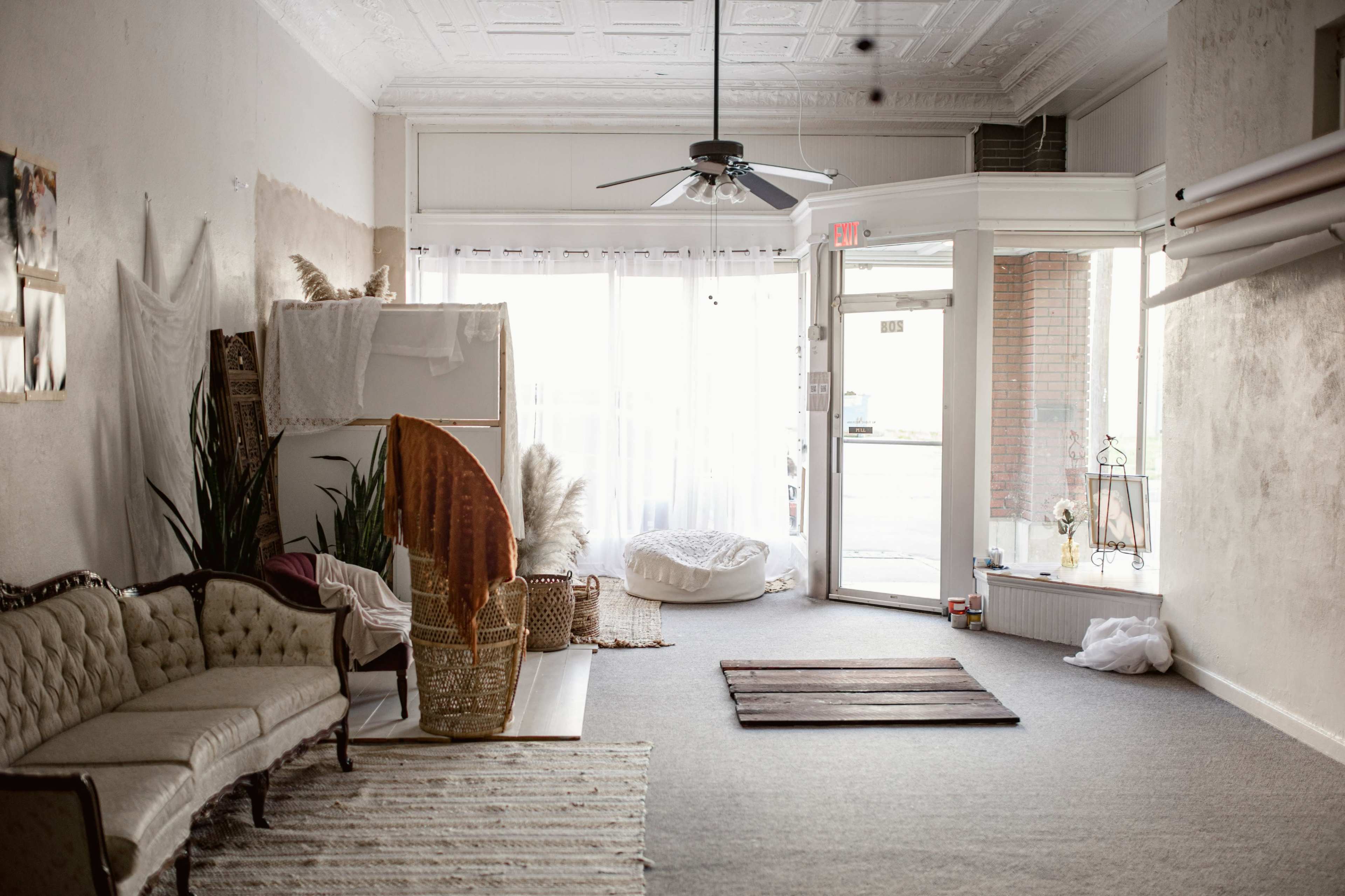 A bright, airy interior of a minimalist room features a vintage couch, indoor plants, and a large entrance with natural light streaming through the windows.