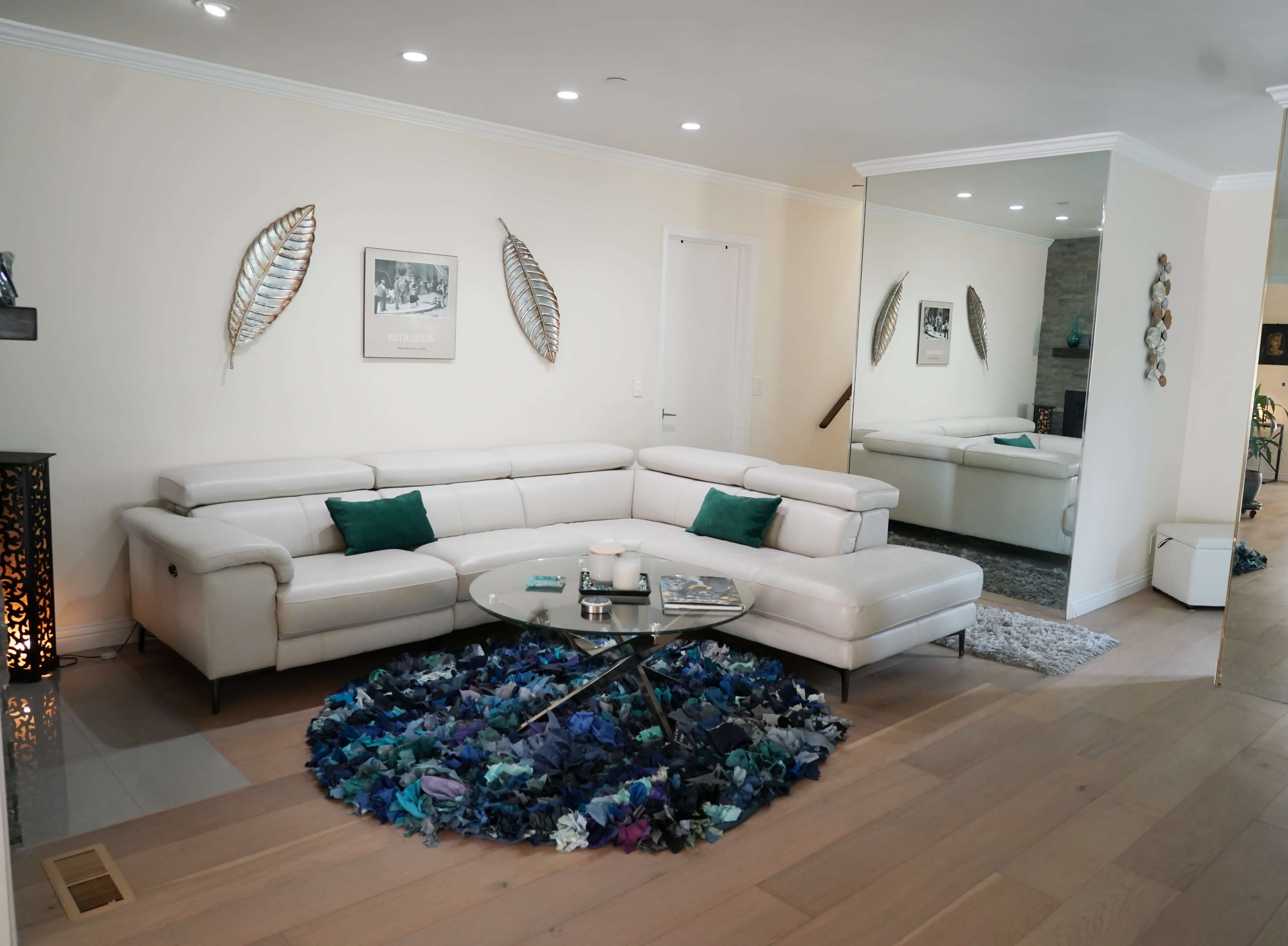 A modern living room featuring a white sectional sofa, a circular coffee table with magazines, and decorative leaf wall art.