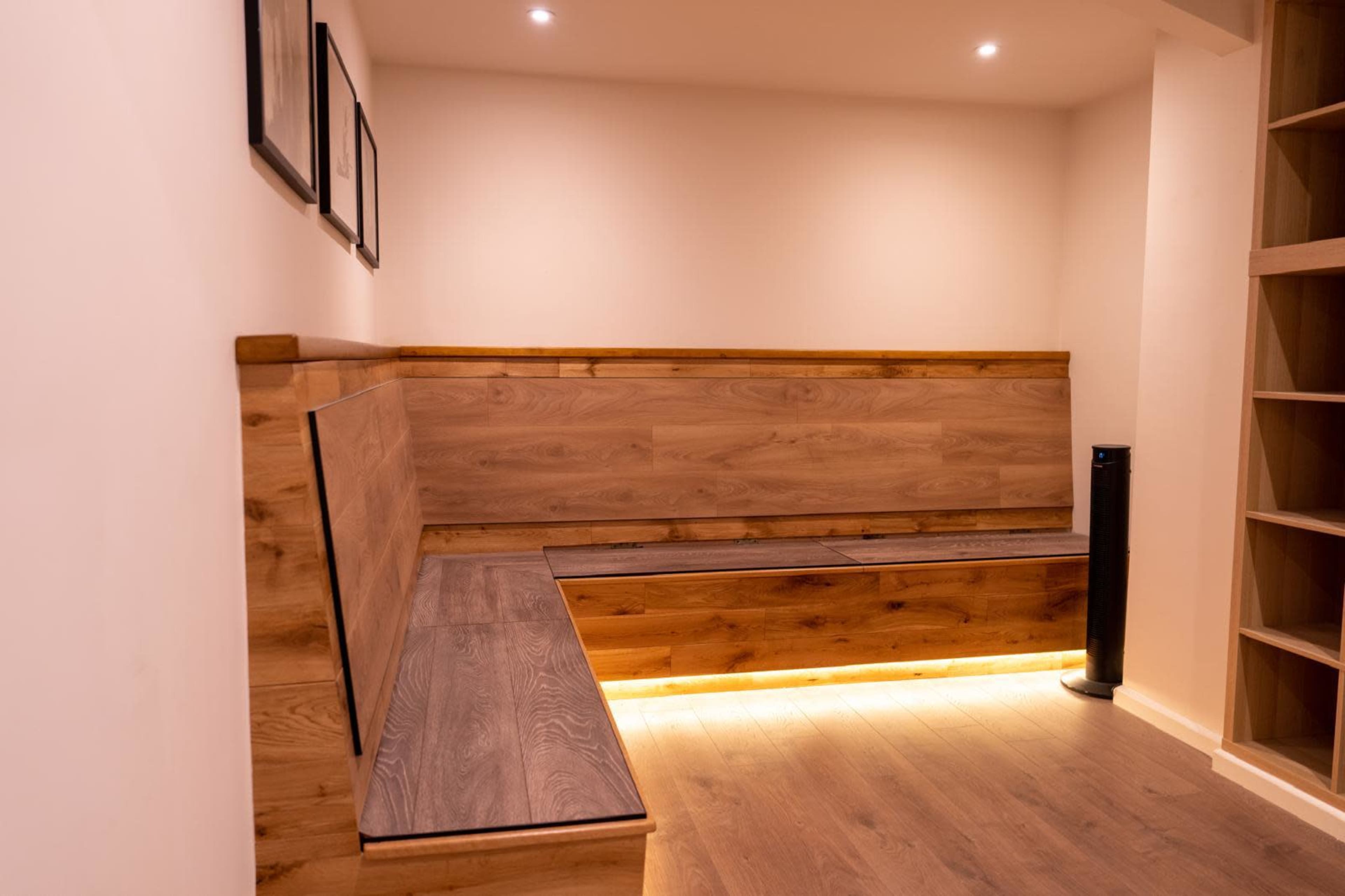 The image shows a minimalist seating area with wooden benches against a softly lit wall.
