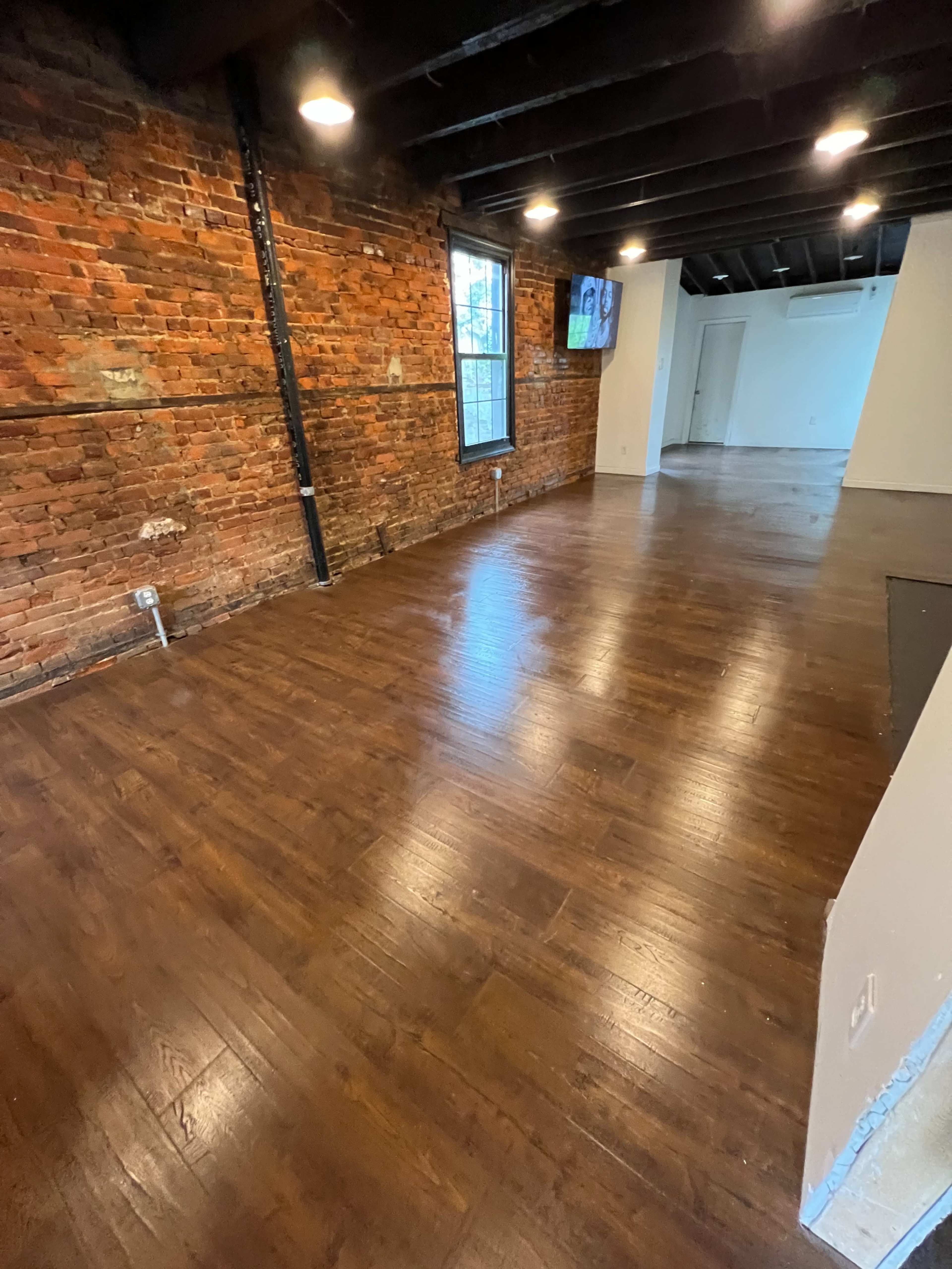 A spacious room with exposed brick walls and polished wooden floors, featuring a television mounted on the wall.