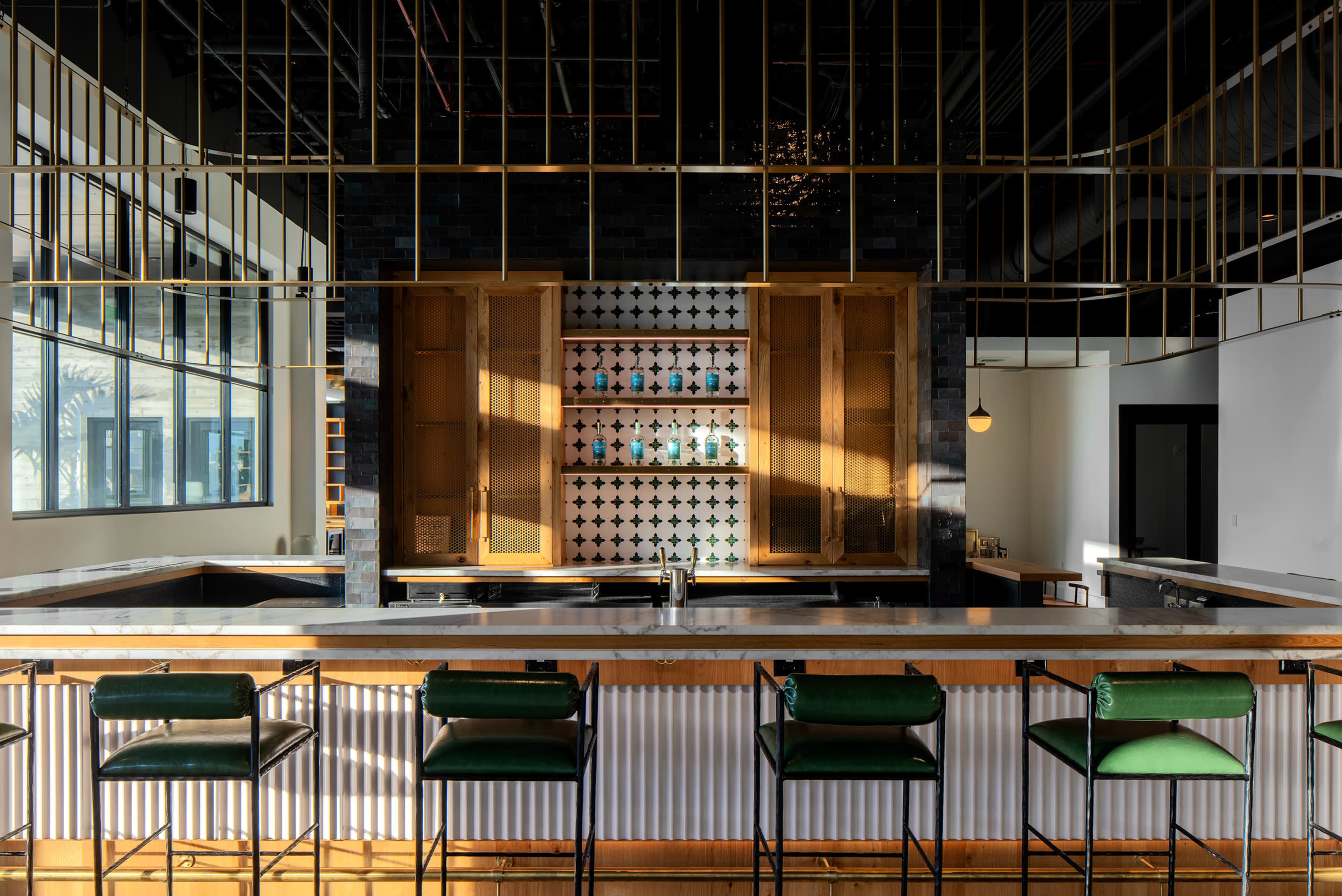 The image features a modern bar area with a polished countertop, green bar stools, and a backdrop displaying shelves illuminated by light.