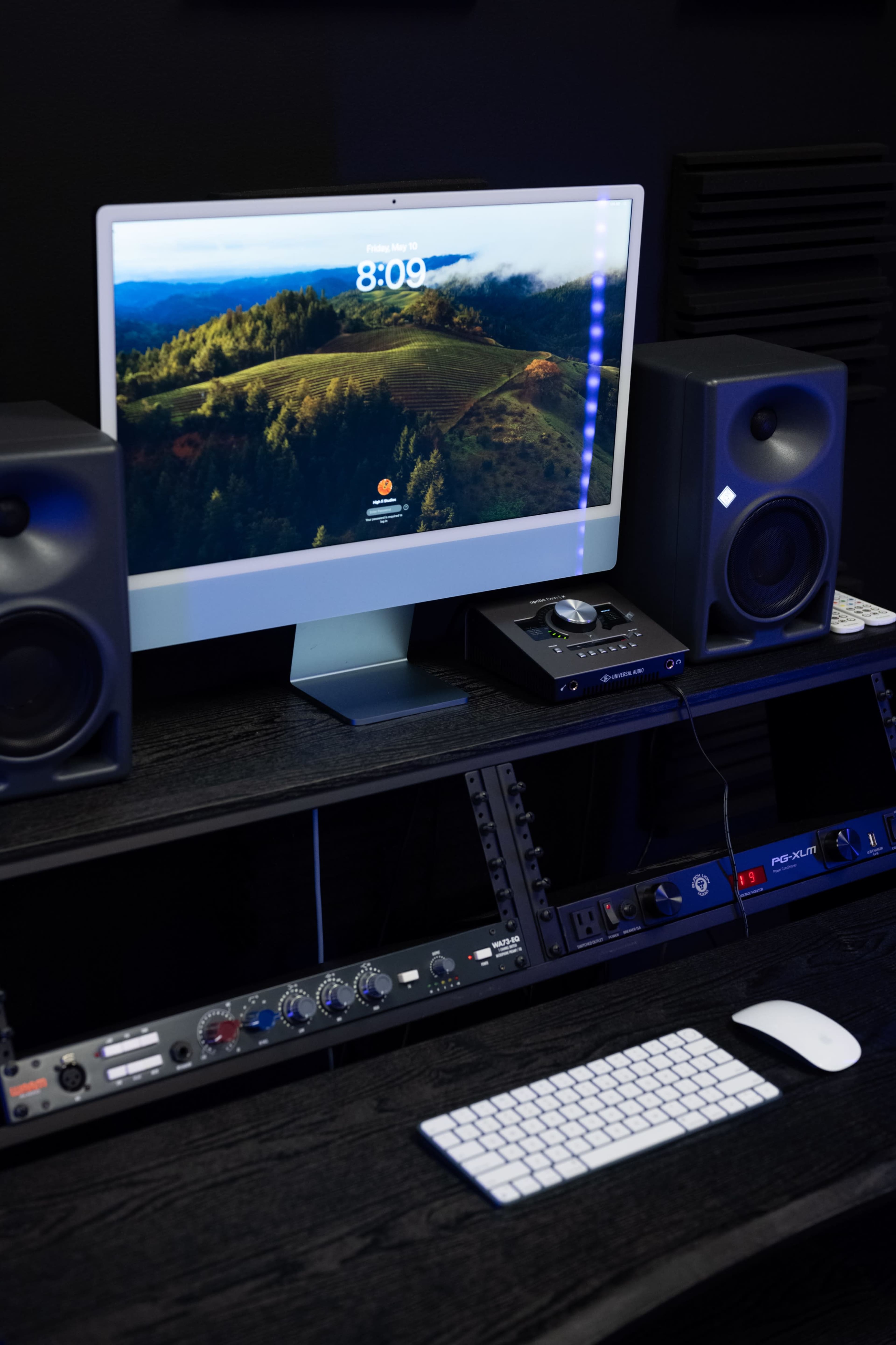 A computer monitor displays a scenic landscape on a desk with audio speakers, a keyboard, and audio equipment.