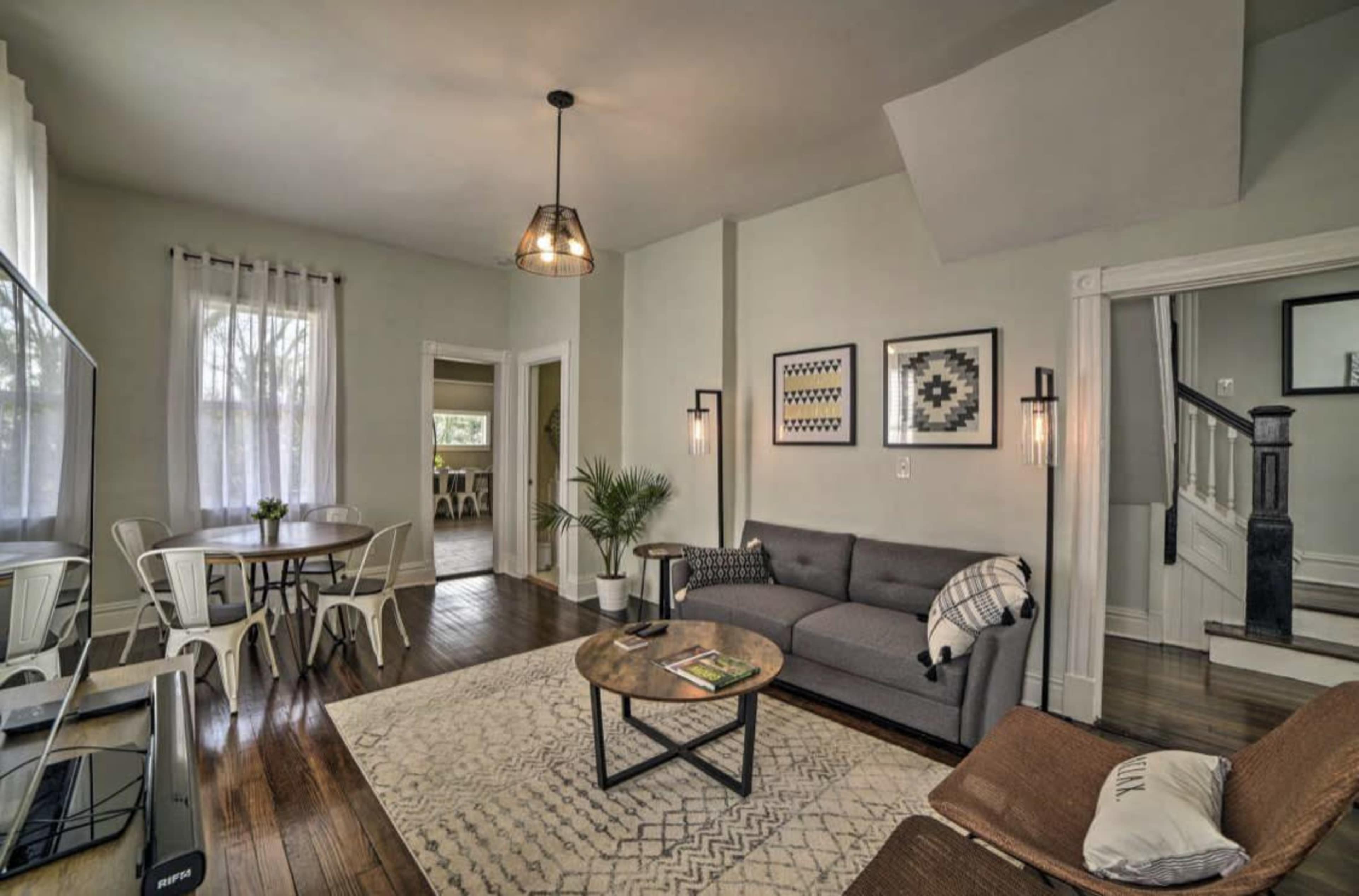 A modern living room with a gray sofa, a round coffee table, a TV, and a dining area in the background.