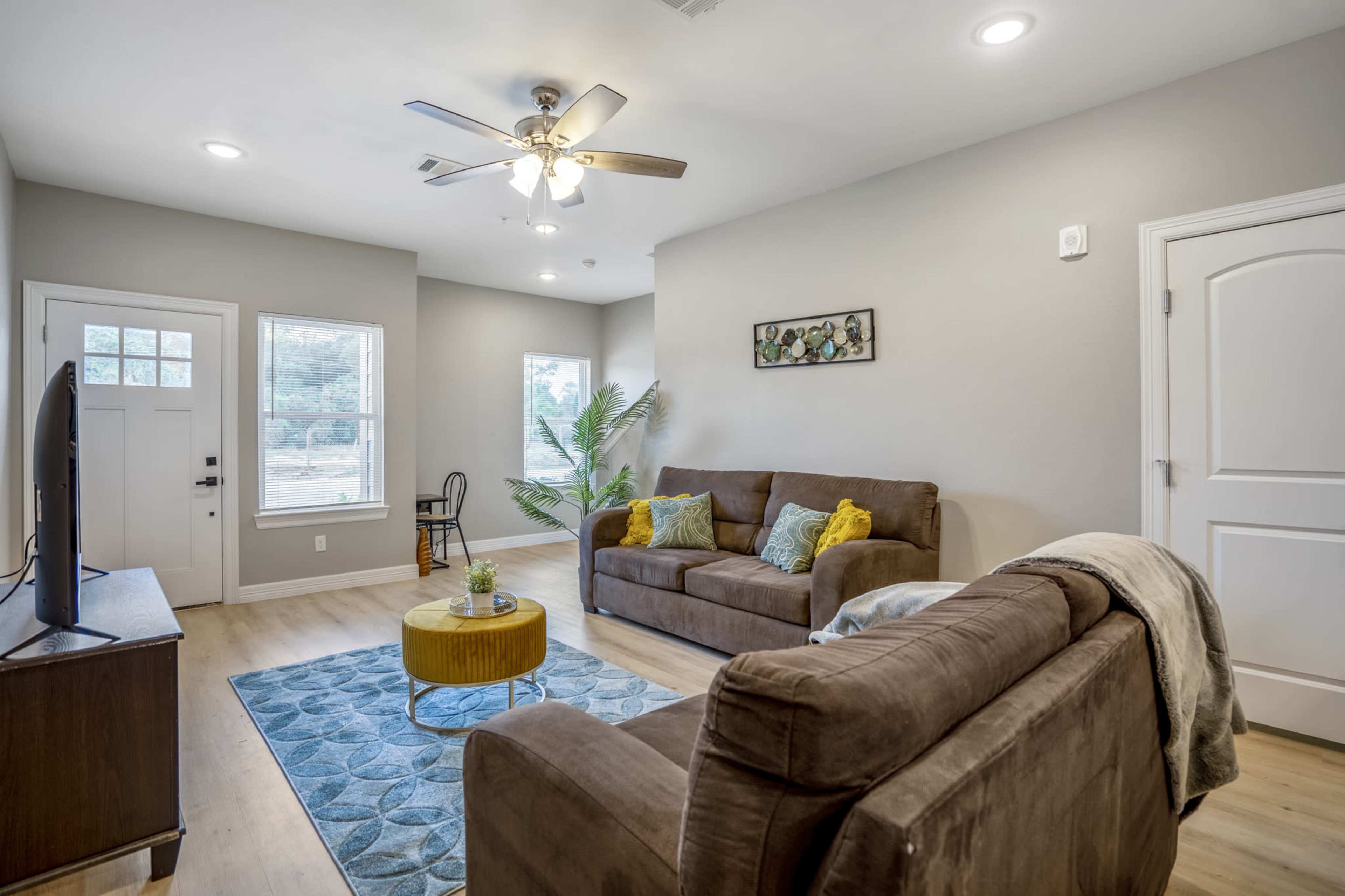A living room features a brown sofa and armchair, a coffee table with a plant, and a window with natural light.