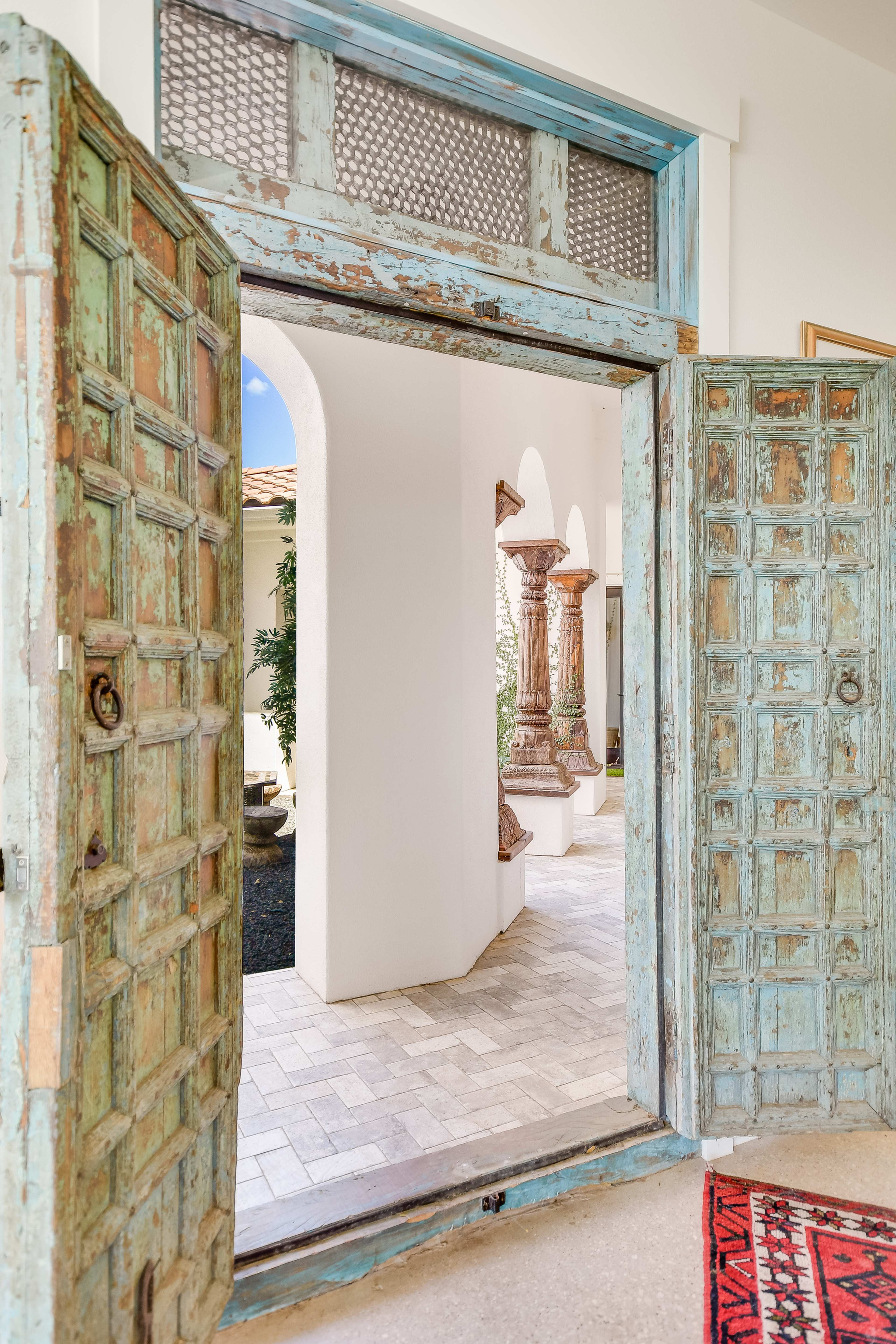 An open turquoise door leading to a tastefully designed interior with patterned flooring and decorative columns visible in the background.