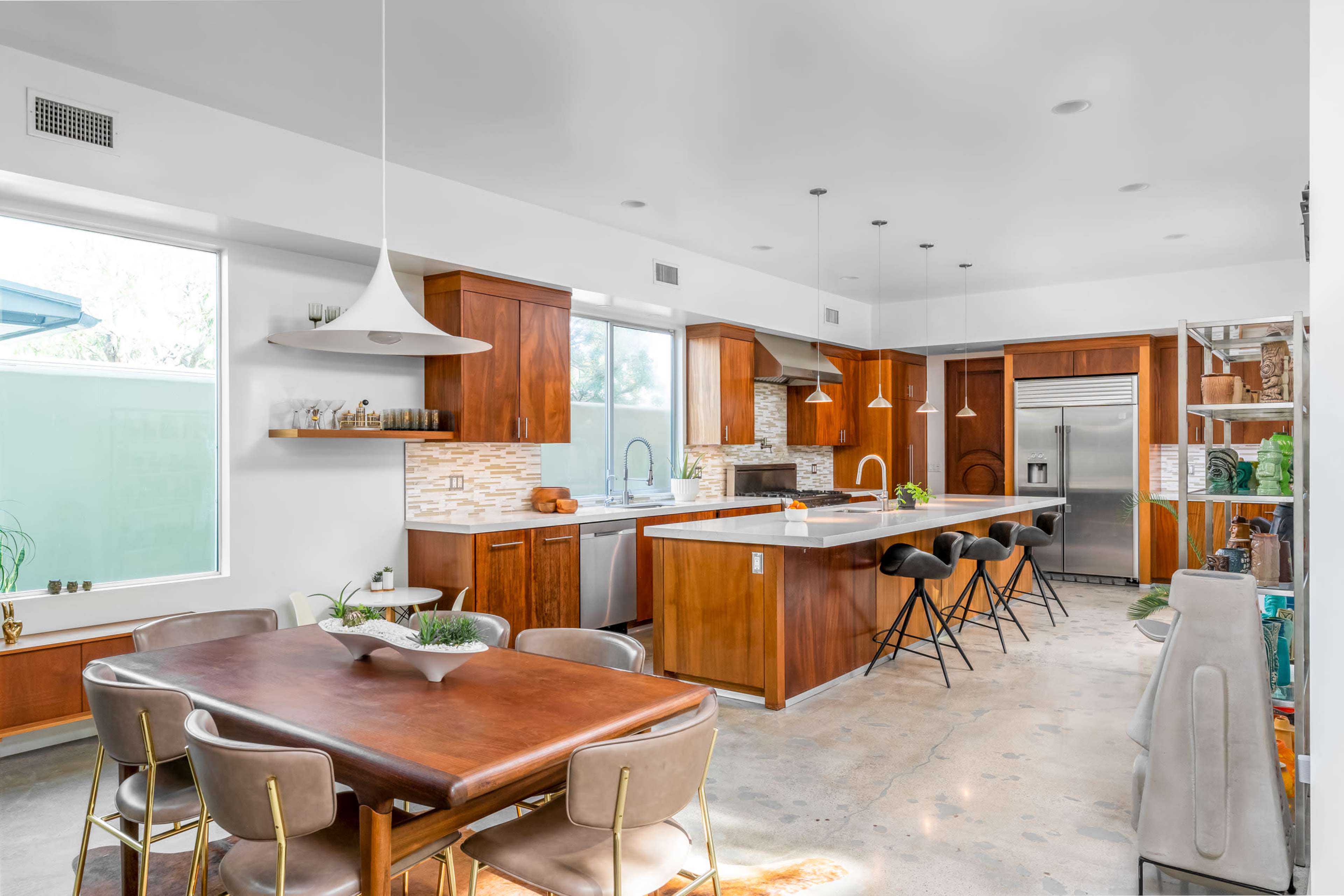 A modern kitchen and dining area feature wooden cabinetry, a large island with seating, and a dining table surrounded by chairs.