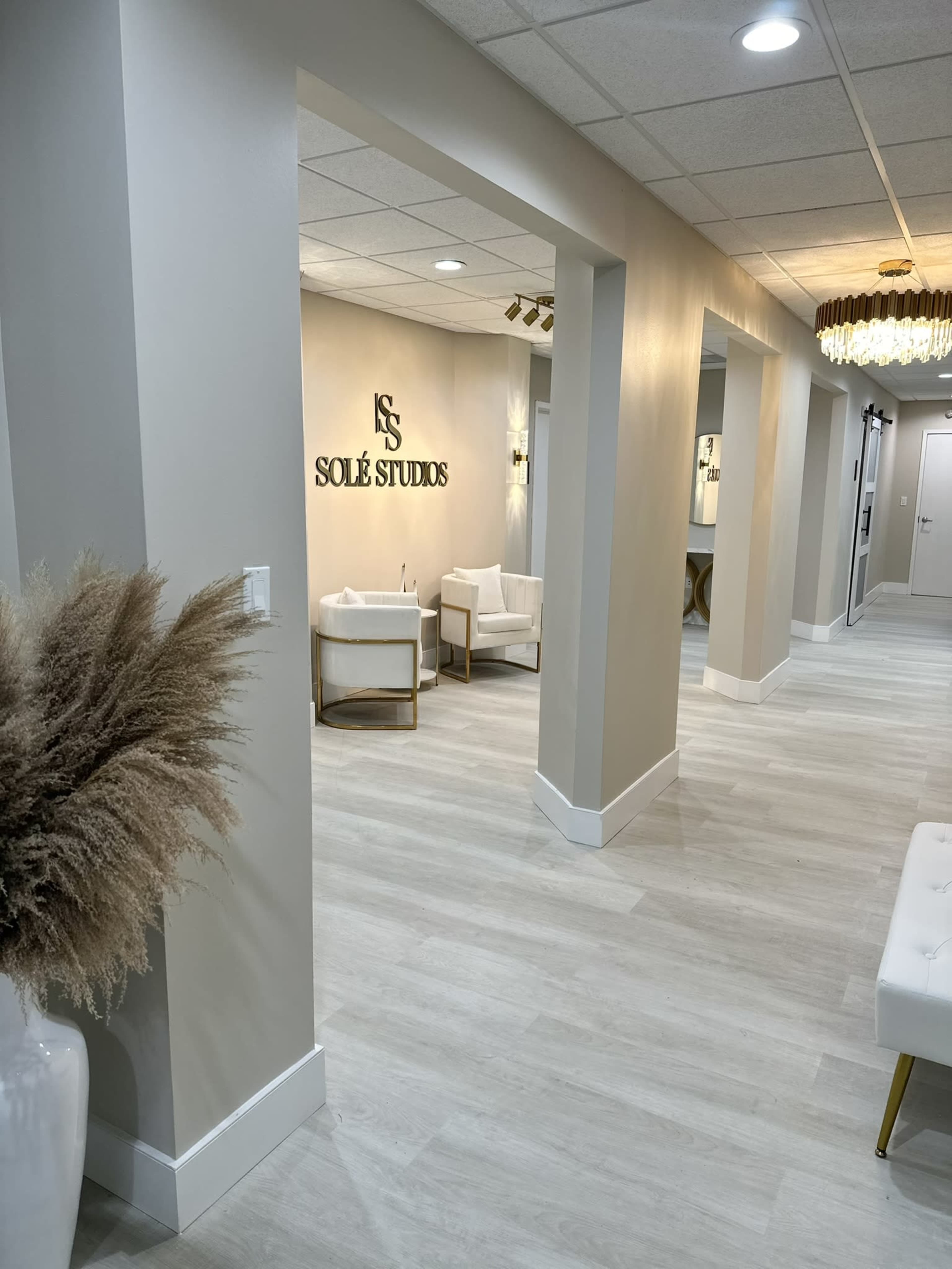 A light-colored hallway with two plush chairs and a decorative plant, leading to a wall displaying the name "SOLE STUDIOS."
