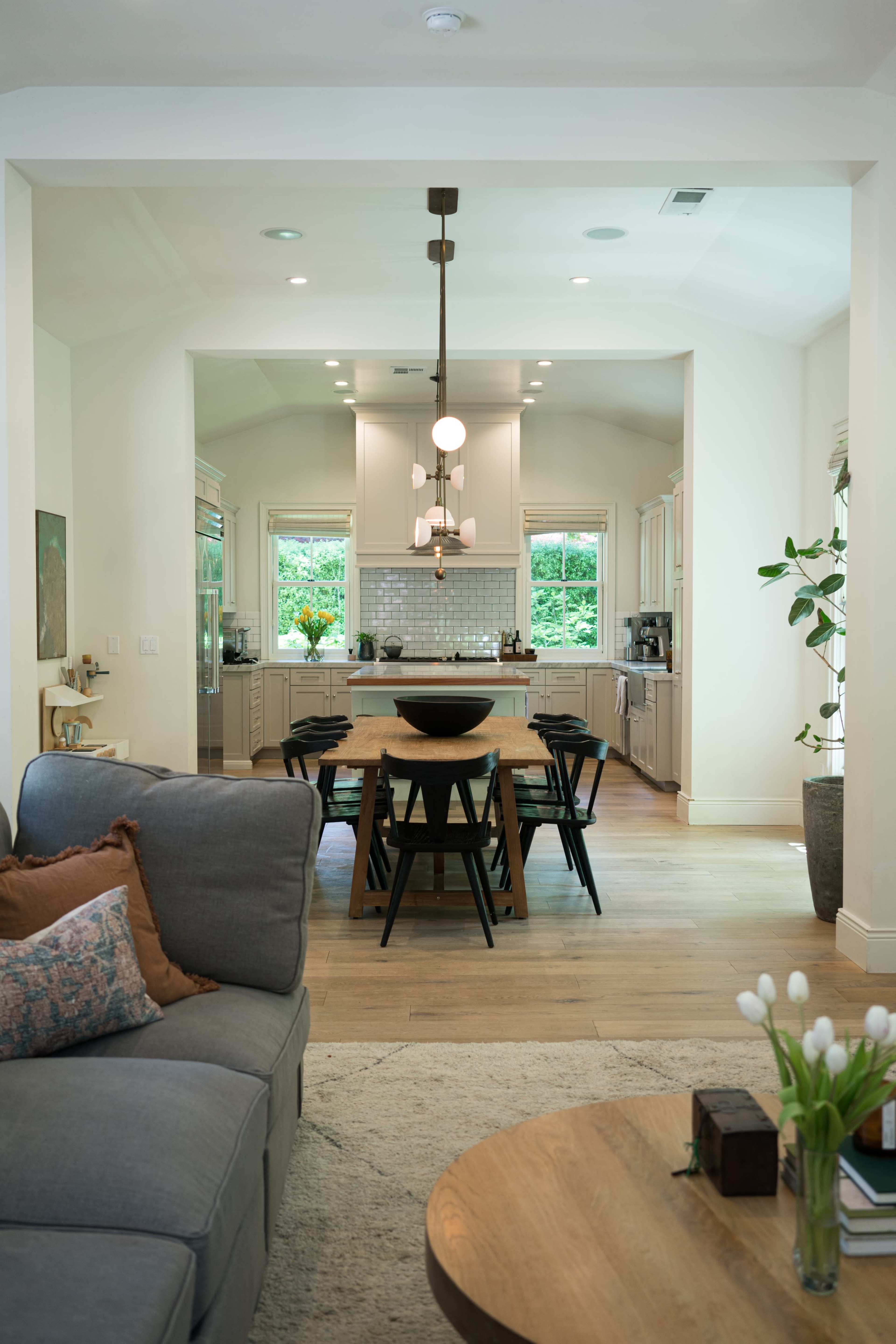 A modern, open-concept kitchen and dining area with a large table, stylish light fixture, and soft seating.