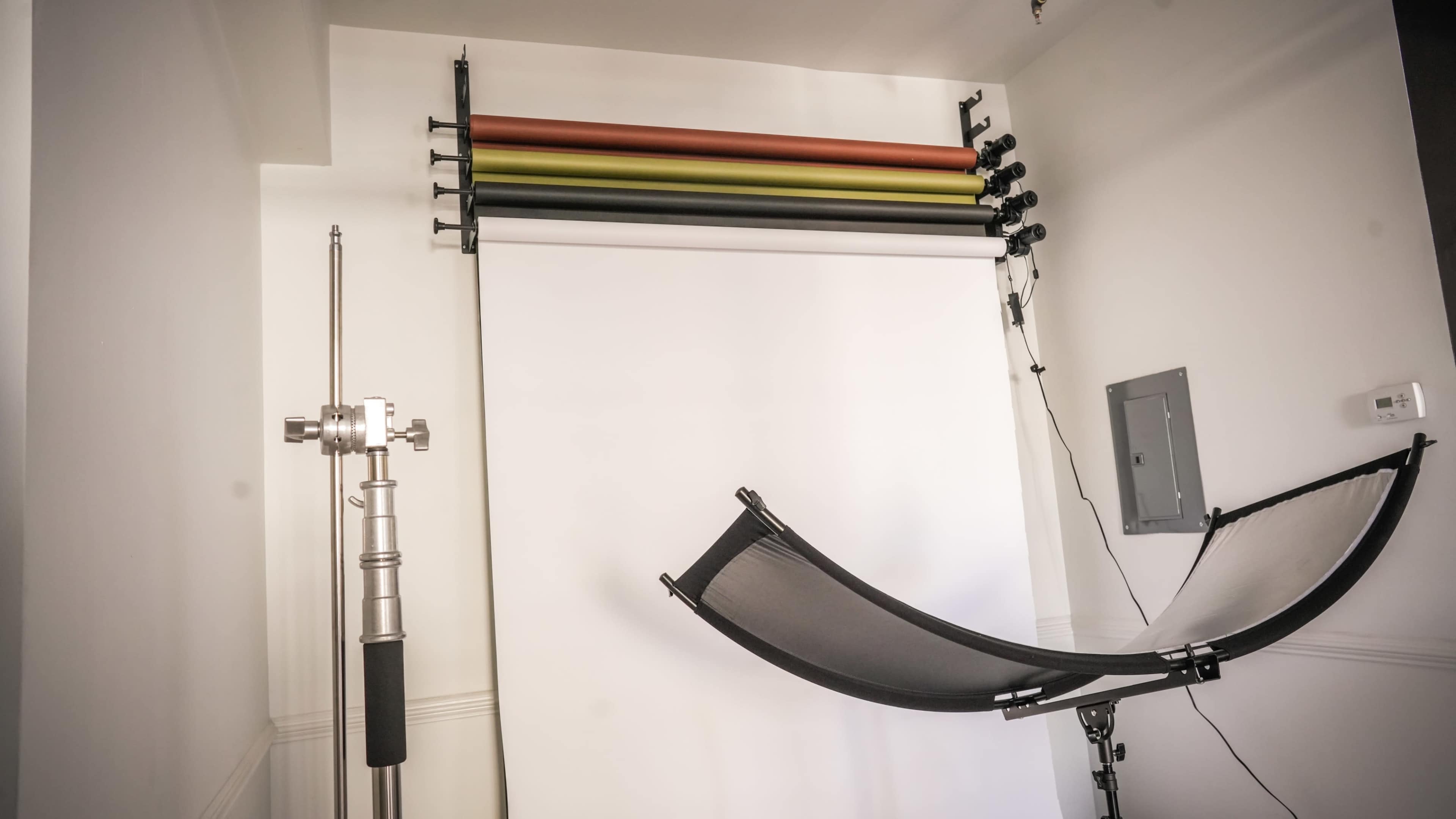 A photo studio setup with a white backdrop, several roll-down colored backdrops, and a support stand for a hammock.