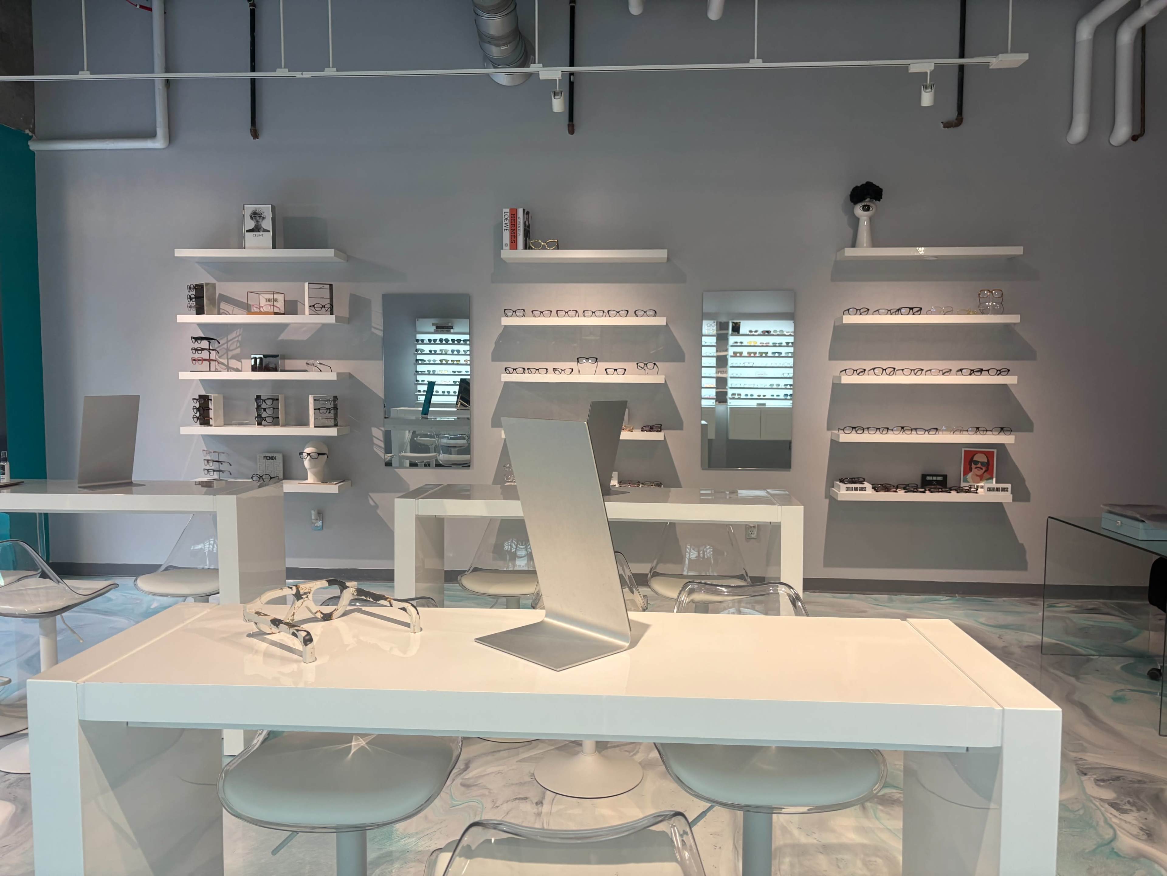 The image shows a modern eyewear store with sleek white tables and shelves displaying various styles of glasses.